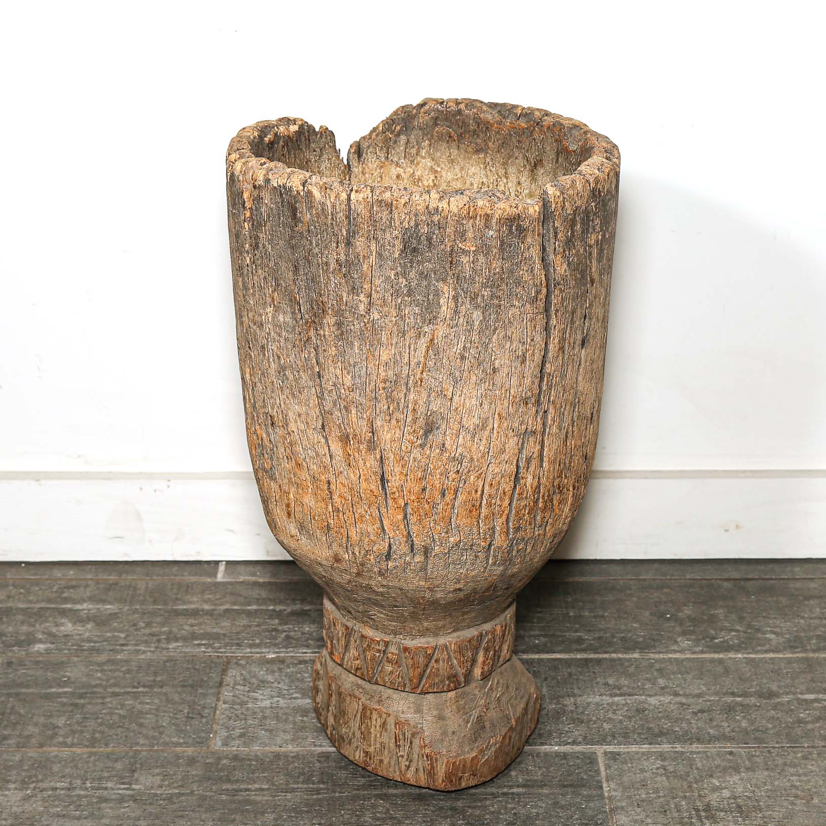 African Wooden vase with a textured surface on a gray floor.