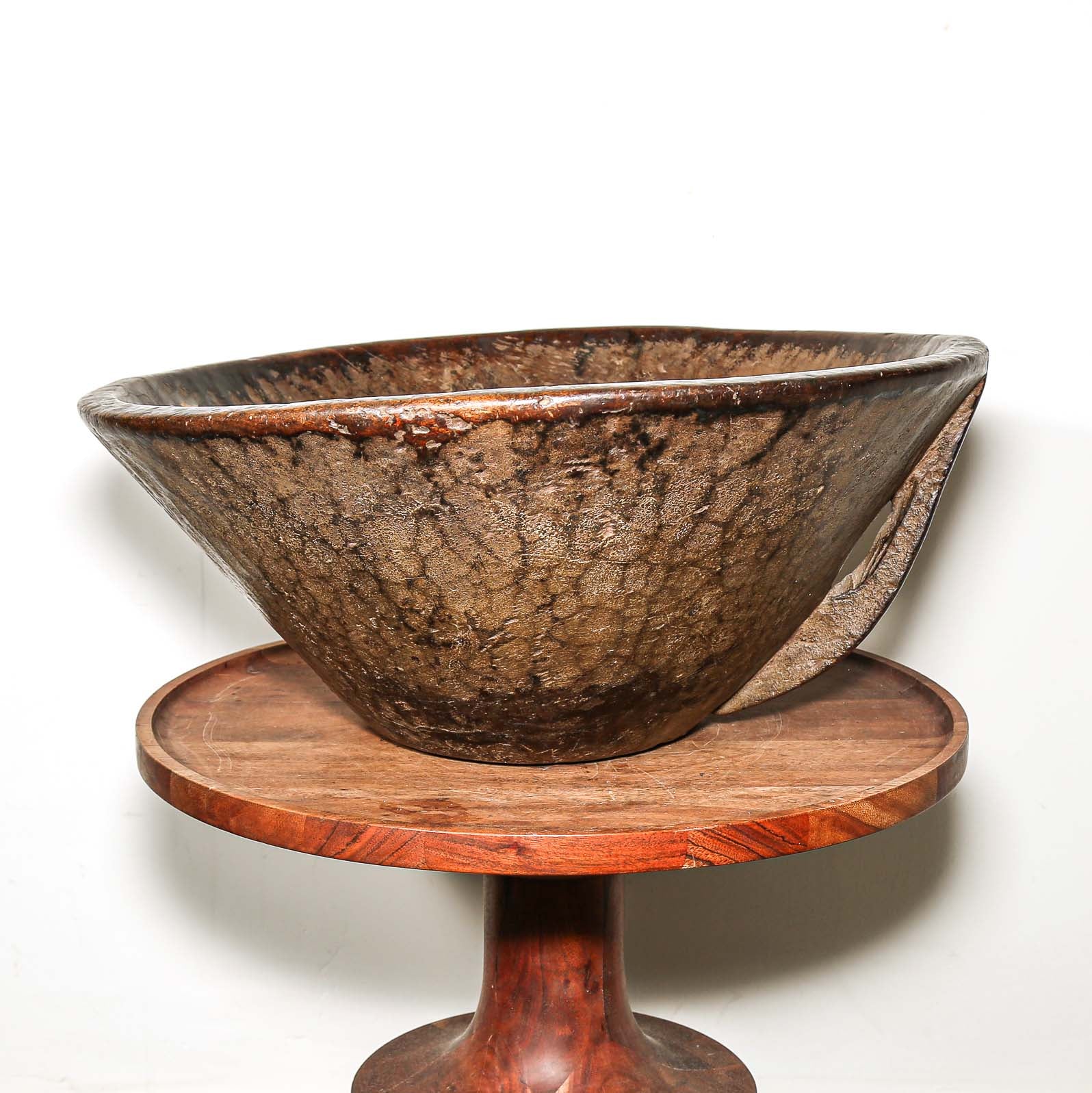 Brown wooden African bowl on a wooden pedestal stand against a white background