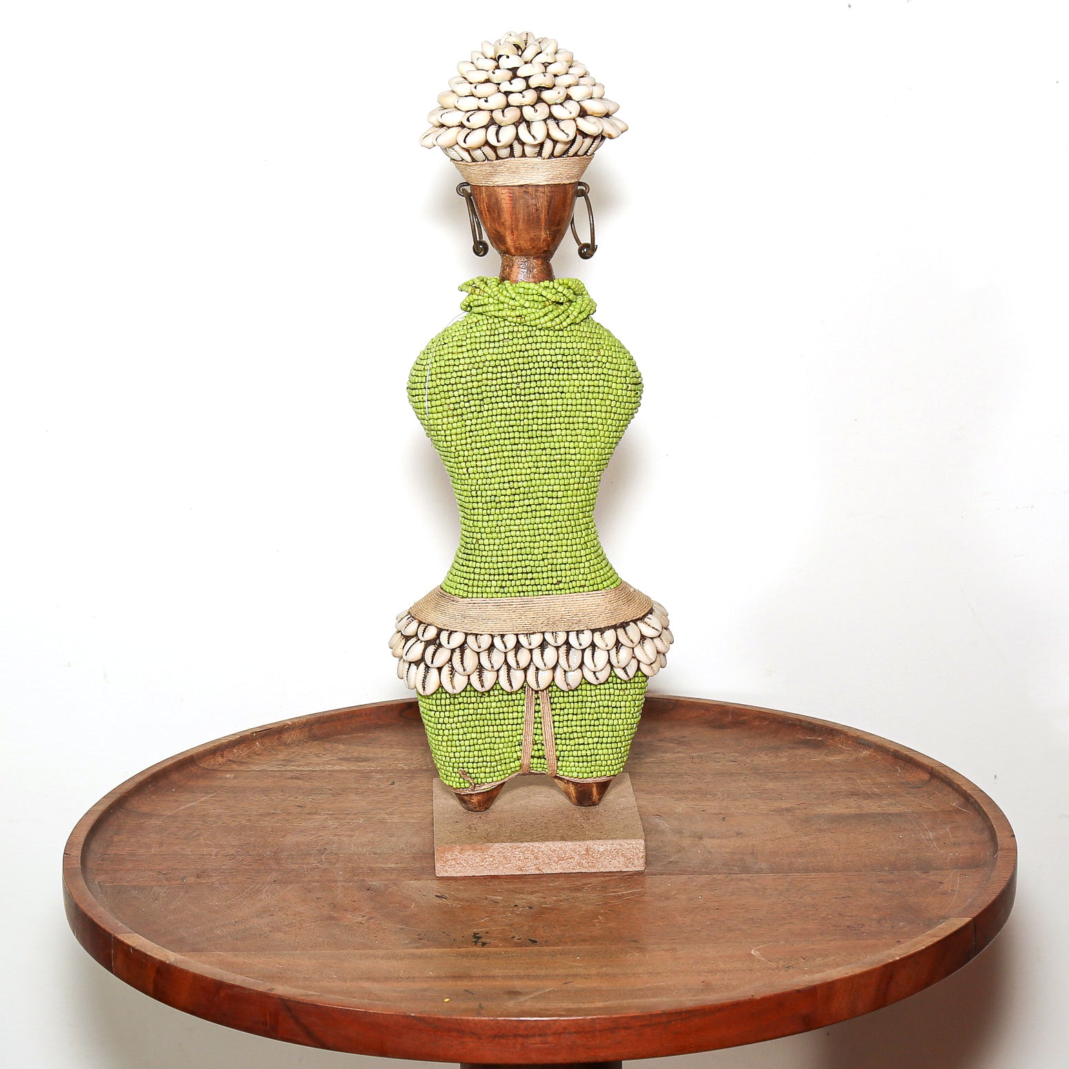 A decorative African-style woven female figurine sculpture displayed on a round wooden tray against a plain white background.