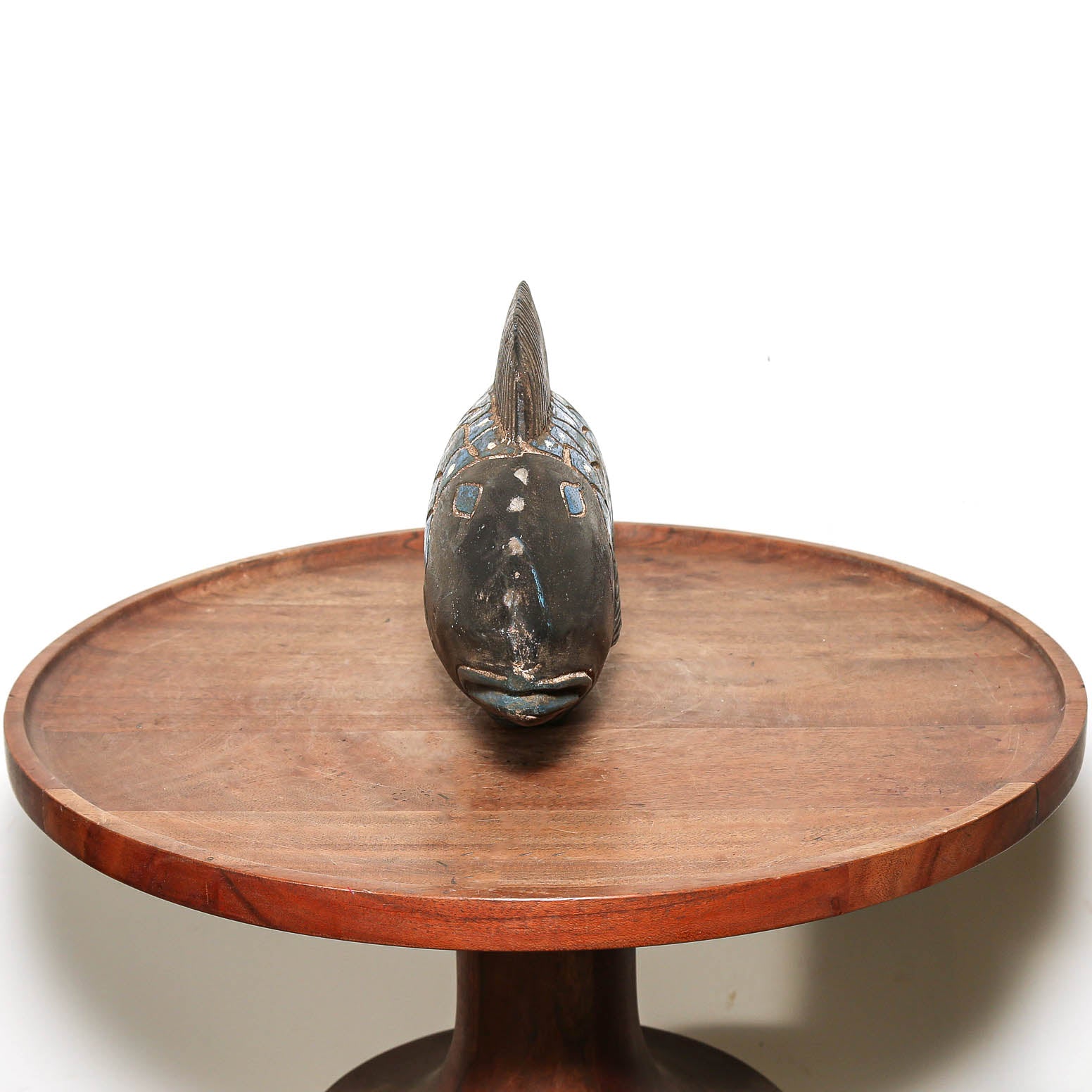 A carved wooden fish-shaped decorative sculpture with blue painted accents, displayed on a round wooden pedestal tray against a plain white background.