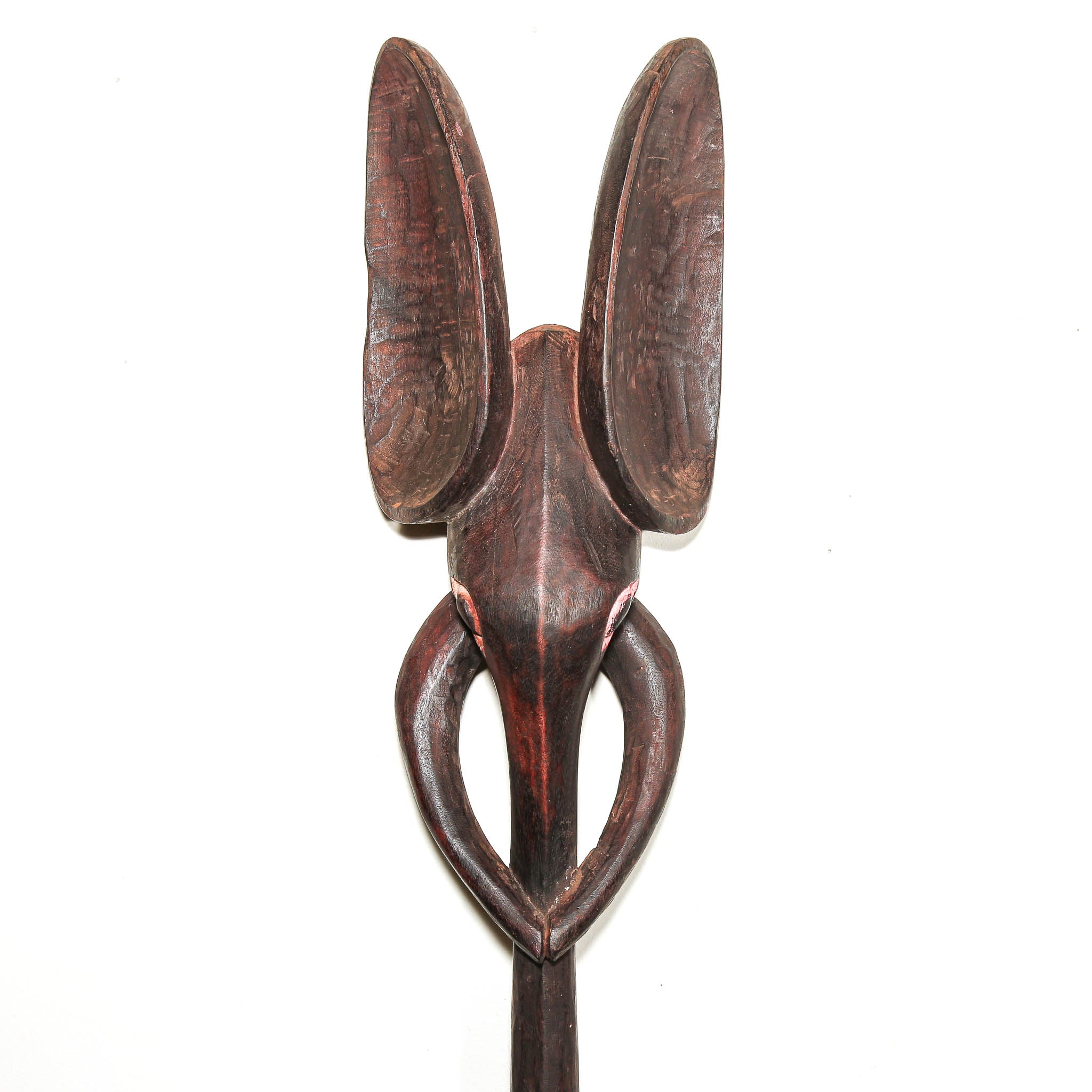 A dark brown carved wooden elephant mask with two upright curved horns or antler-like shapes and a looped base, photographed against a plain white background.