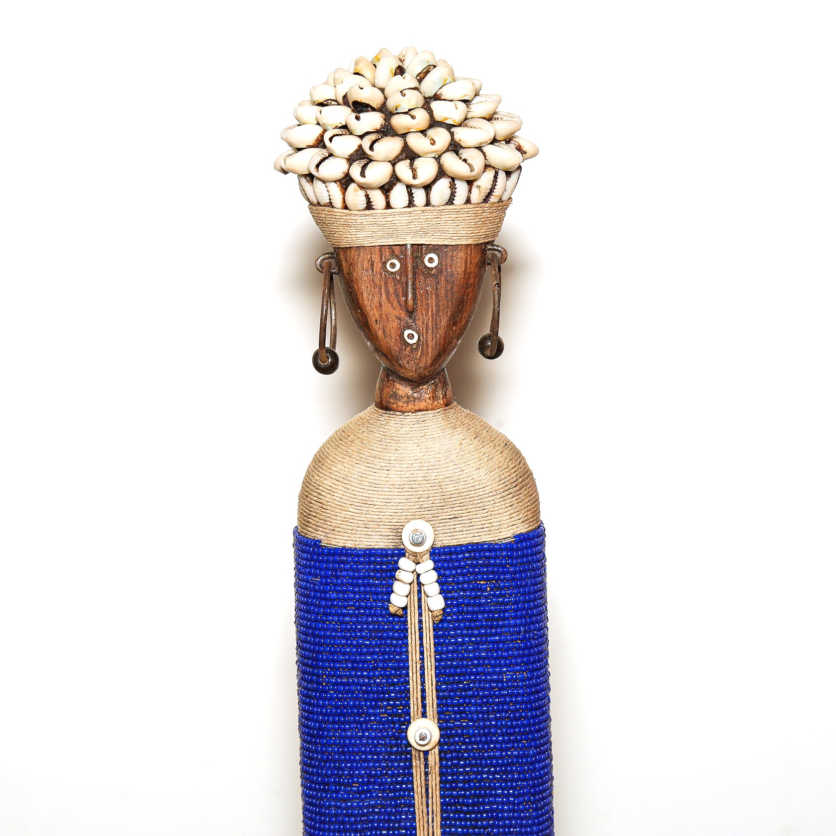 A handmade African-style wooden figurine of a woman with a brown wood face, a beige woven body, a blue beaded skirt, and a crown made of white cowrie shells, set against a plain white background.