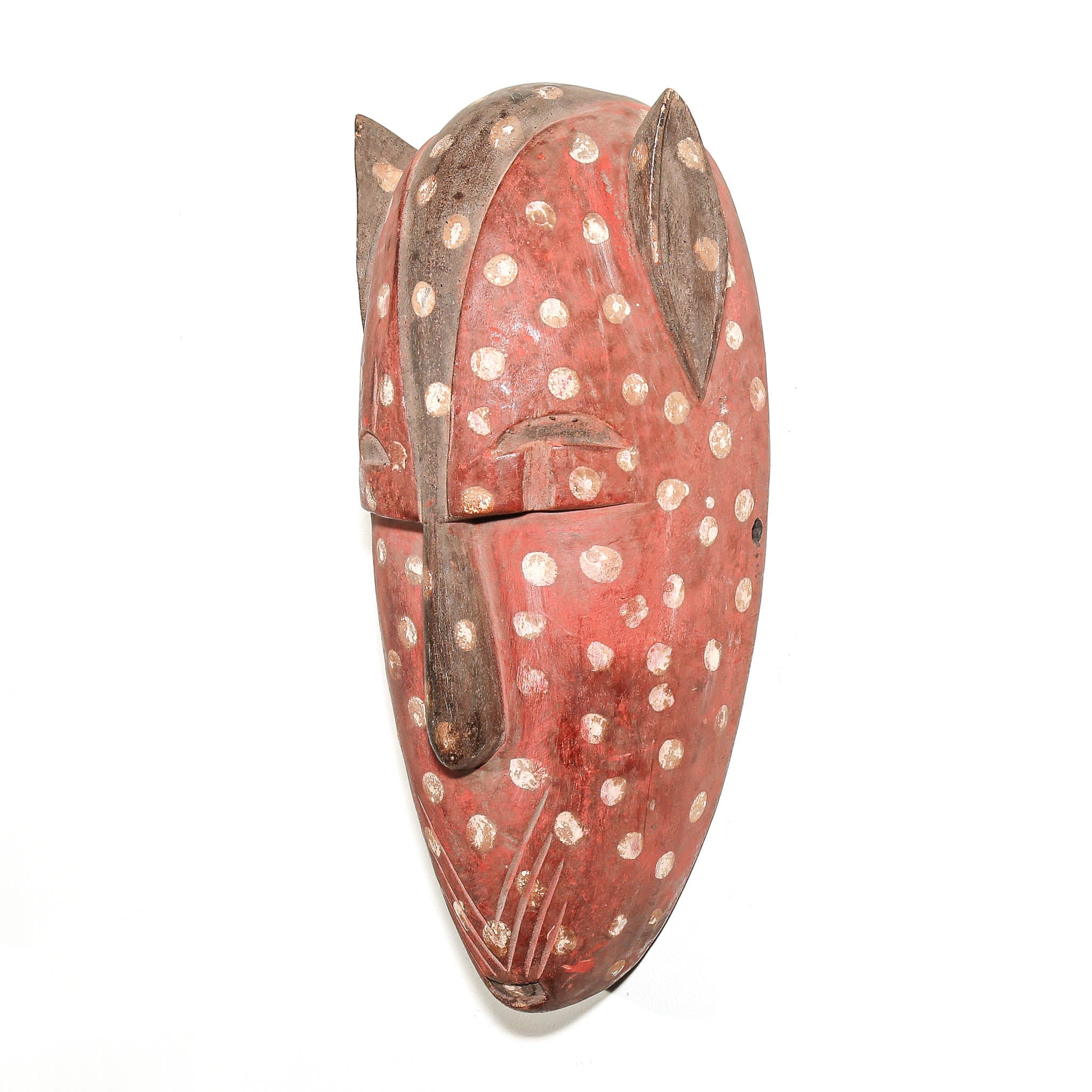 A carved wooden mask with a reddish-pink body, decorated with white speckled dots and dark brown painted details, shown against a plain white background.