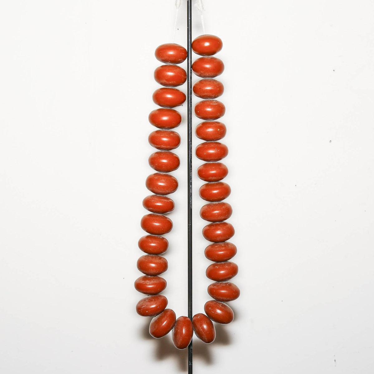 A pair of long strands of polished red coral beads hanging vertically against a plain white background.