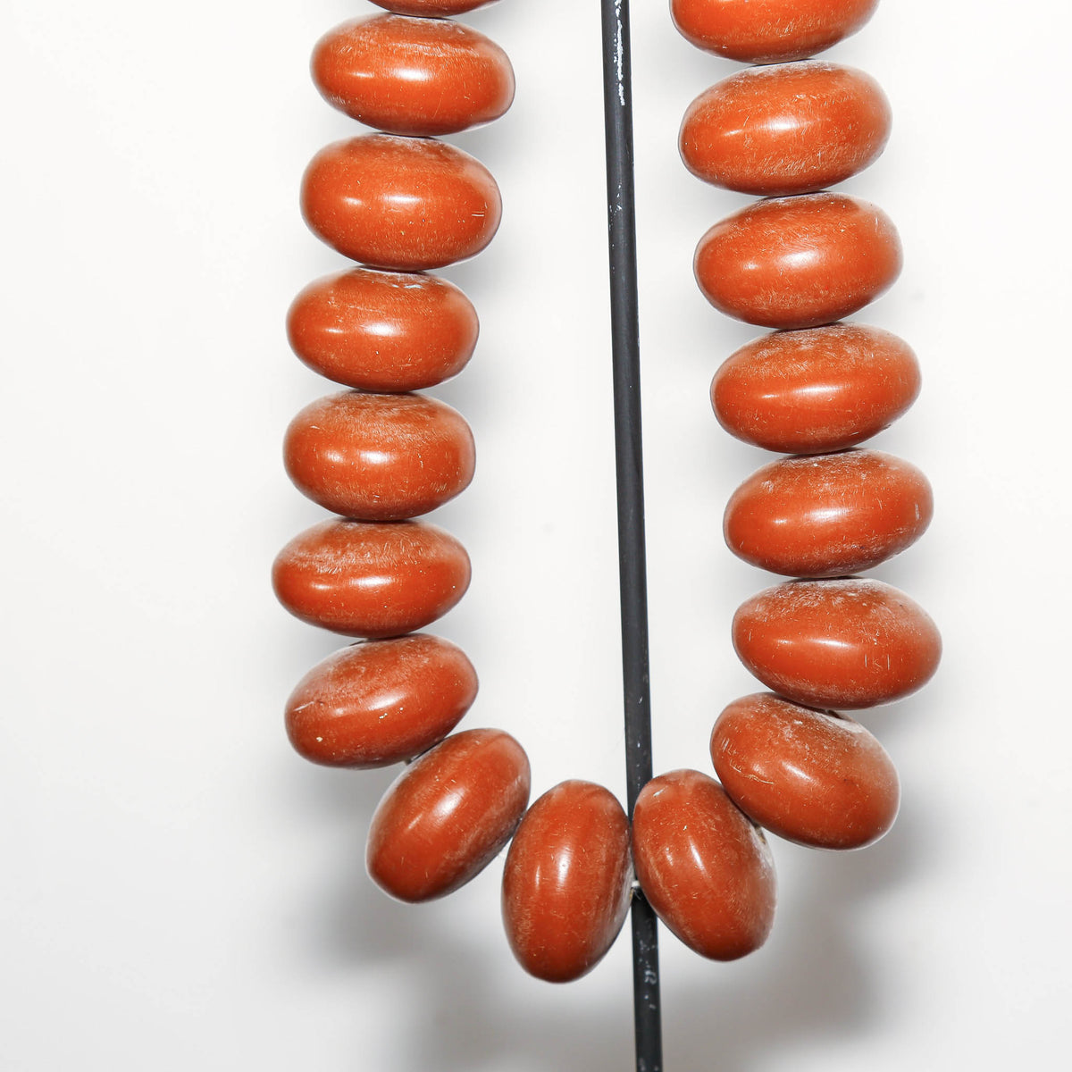 A strand of polished reddish-brown oval beads strung on a black display rod against a plain white background.