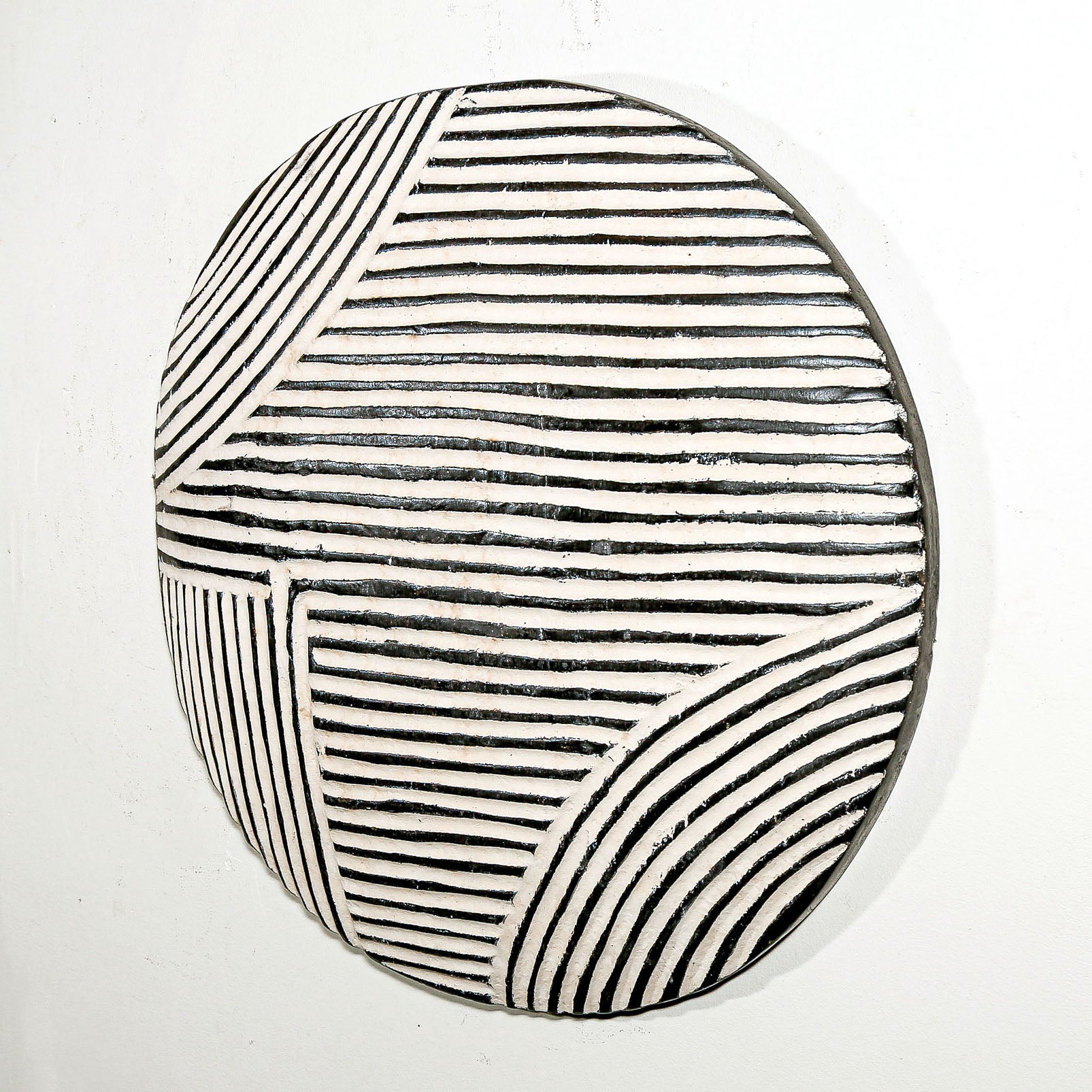 Round wood wall decor with rustic African traditional striped pattern on a white living room wall