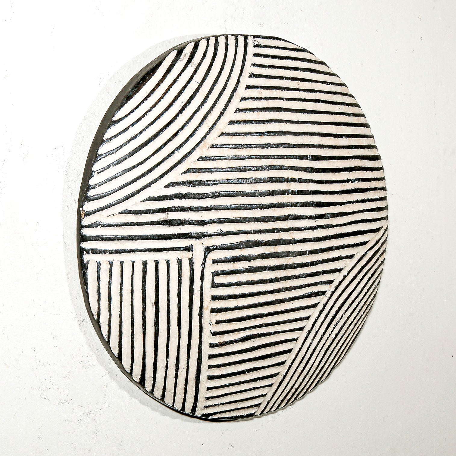 Round wood wall decor with rustic African traditional striped pattern on a white living room wall