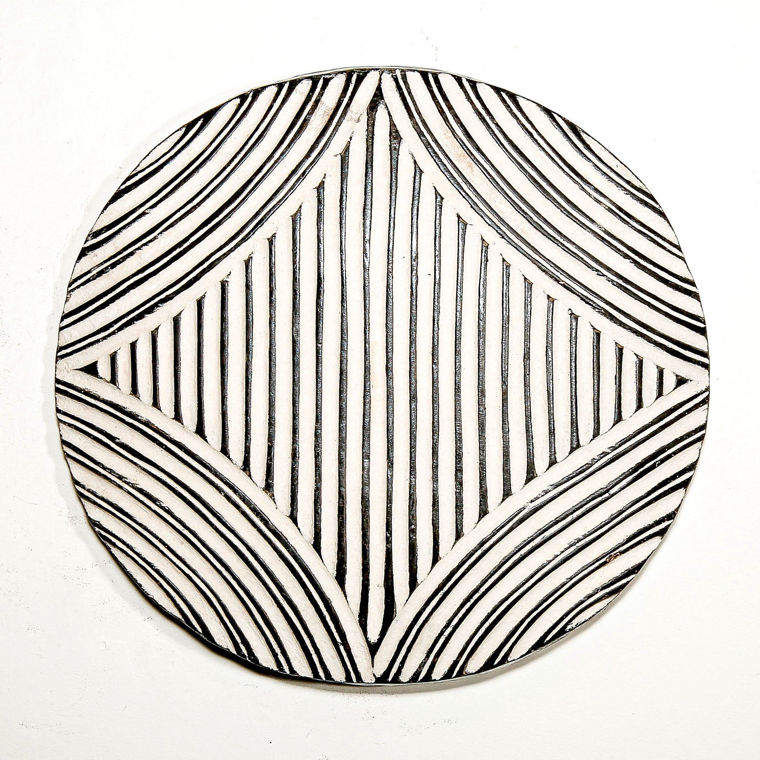 Round wood wall decor with rustic African traditional striped pattern on a white living room wall