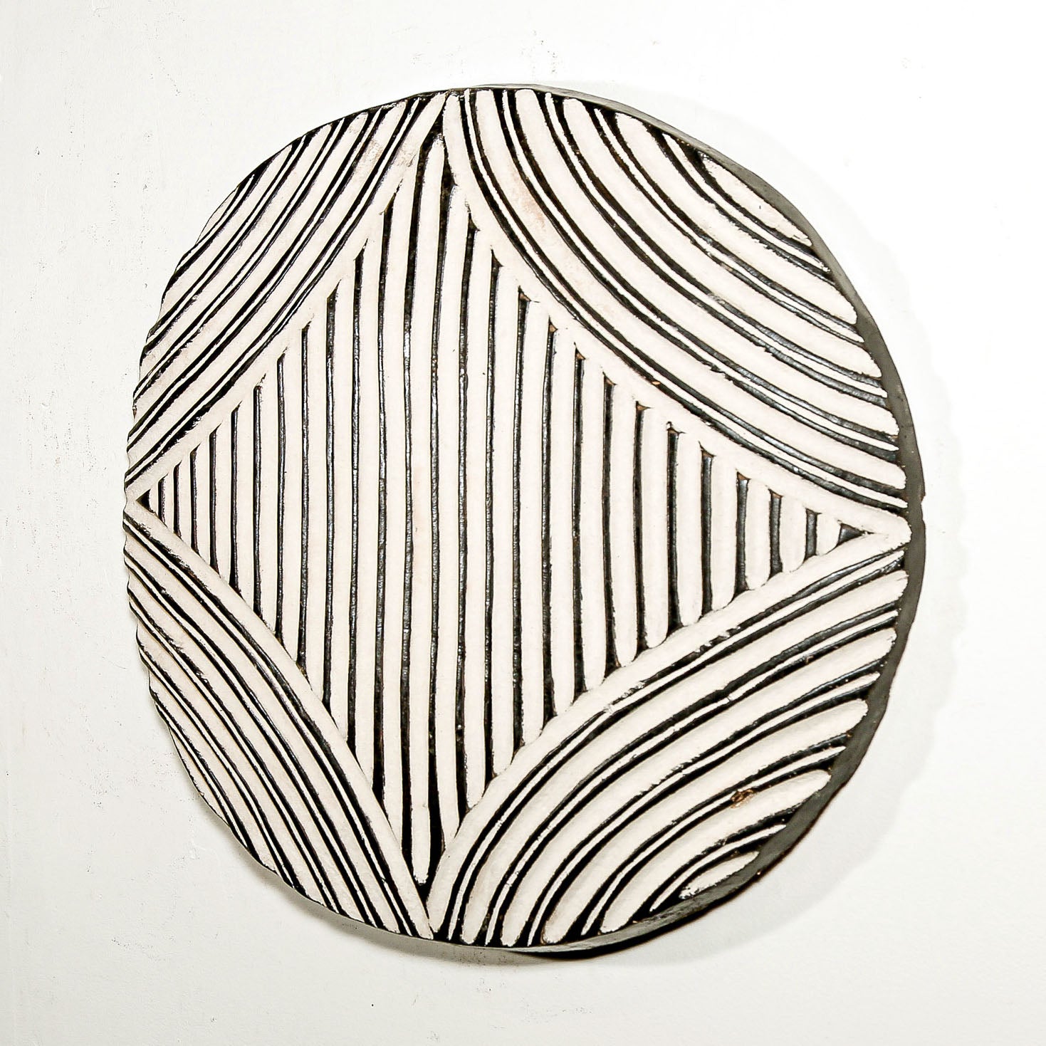 Round wood wall decor with rustic African traditional striped pattern on a white living room wall