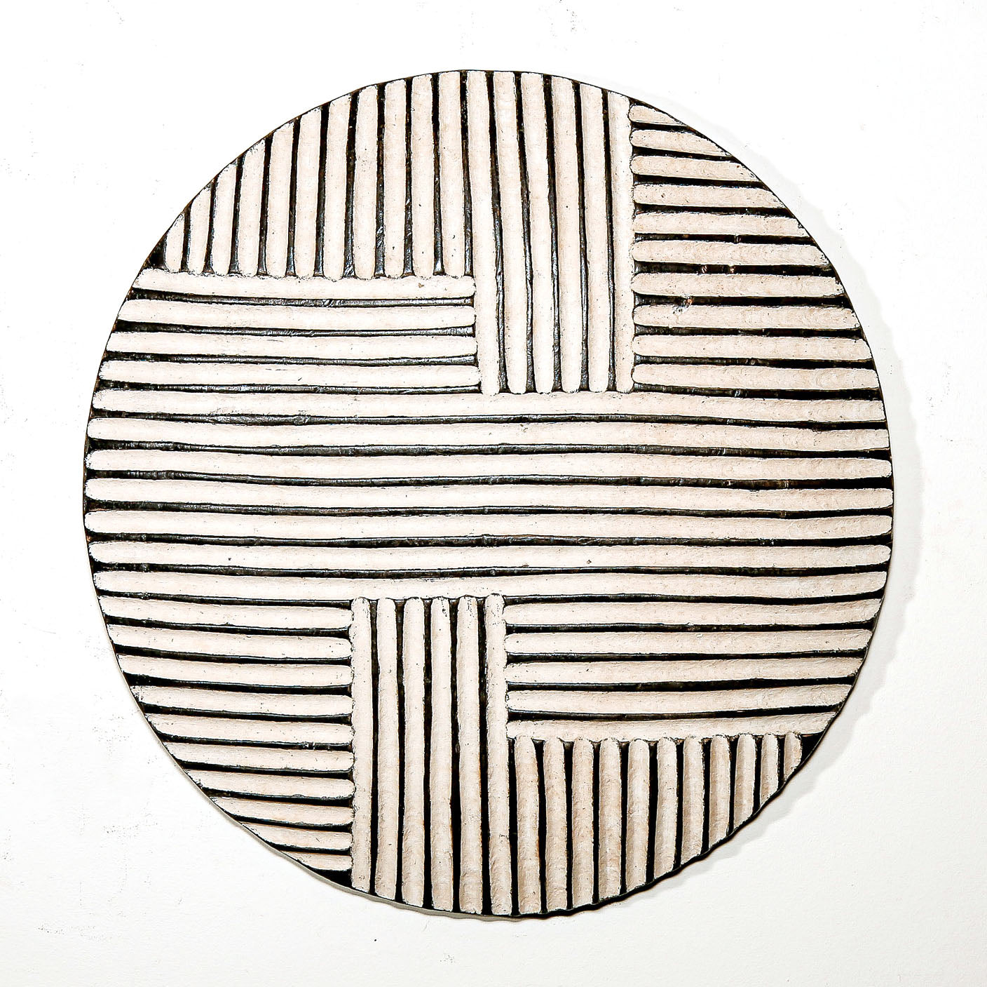 Round wood wall decor with rustic African traditional striped pattern on a white living room wall