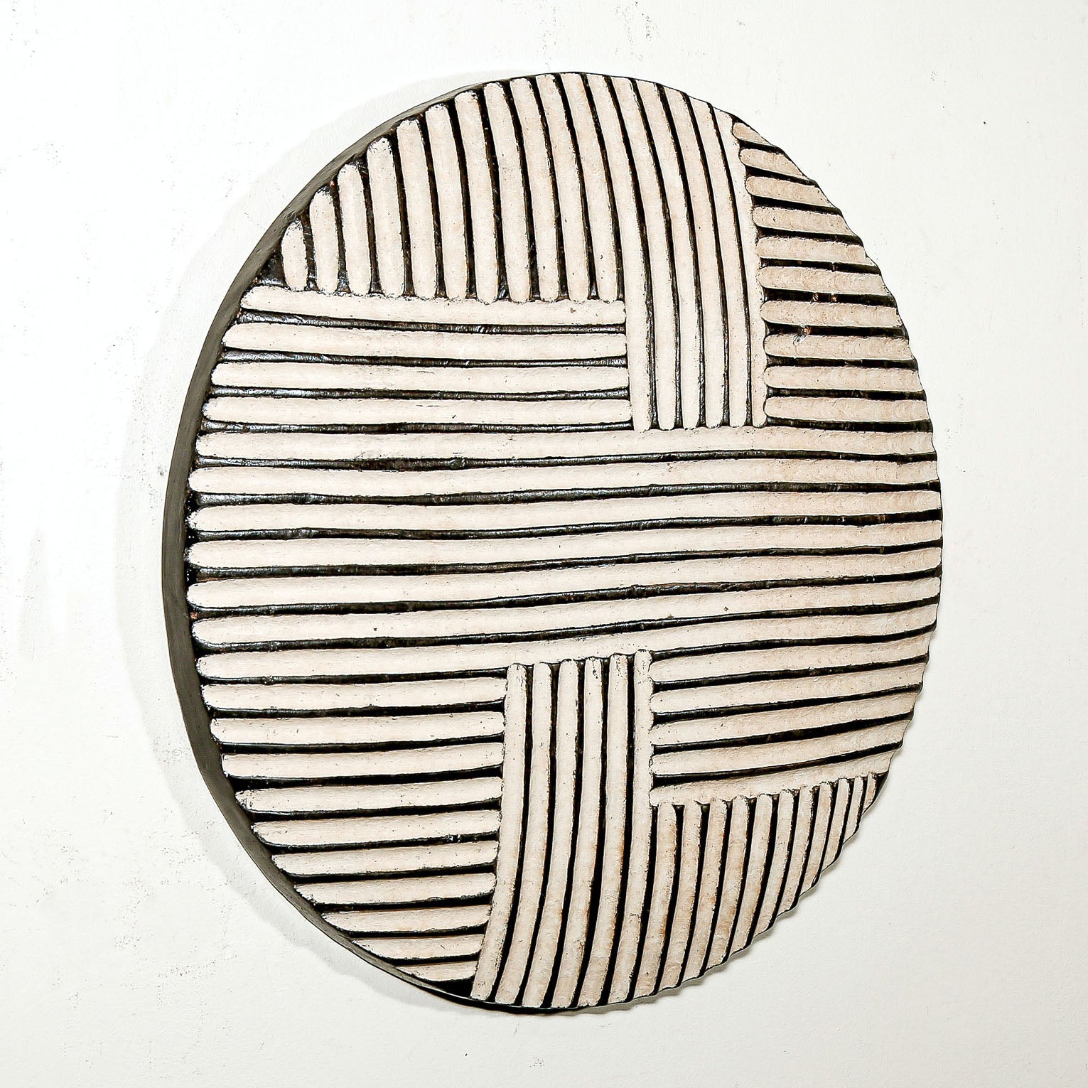 Round wood wall decor with rustic African traditional striped pattern on a white living room wall