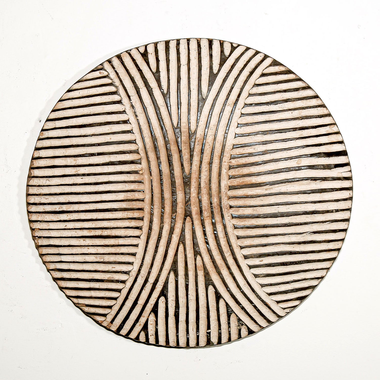 Round wood wall decor with rustic African traditional striped pattern on a white living room wall