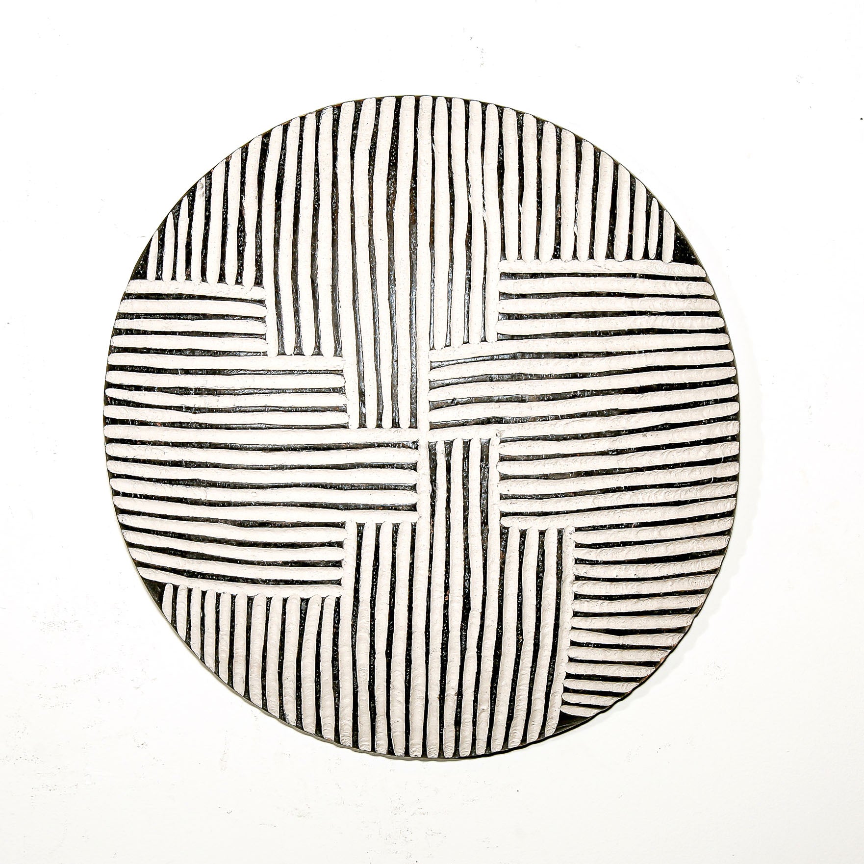 Round wood wall decor with rustic African traditional striped pattern on a white living room wall