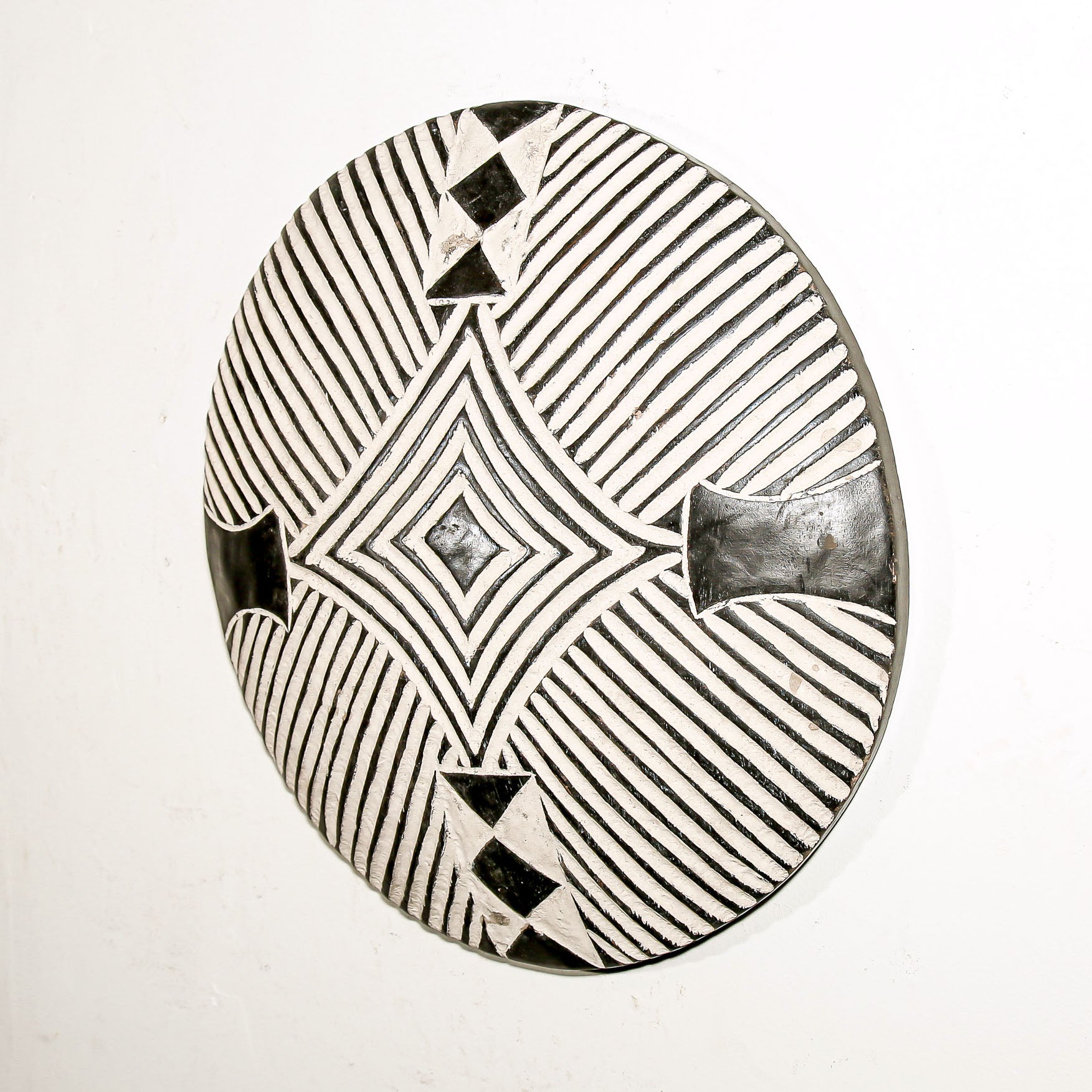 Round wood wall decor with rustic African traditional striped pattern on a white living room wall