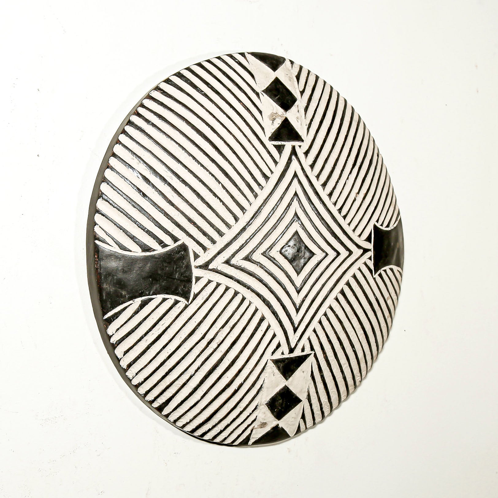 Round wood wall decor with rustic African traditional striped pattern on a white living room wall