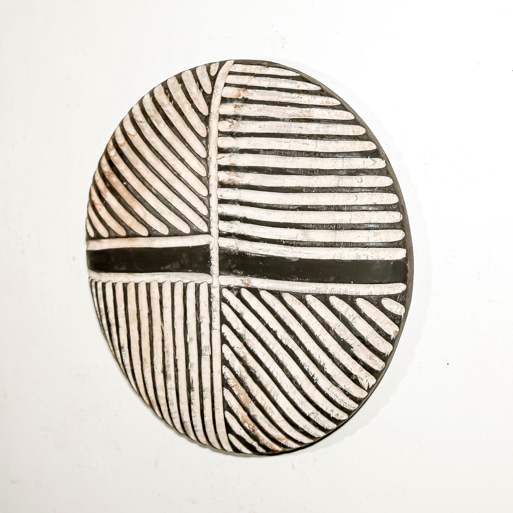 Round wood wall decor with rustic African traditional striped pattern on a white living room wall