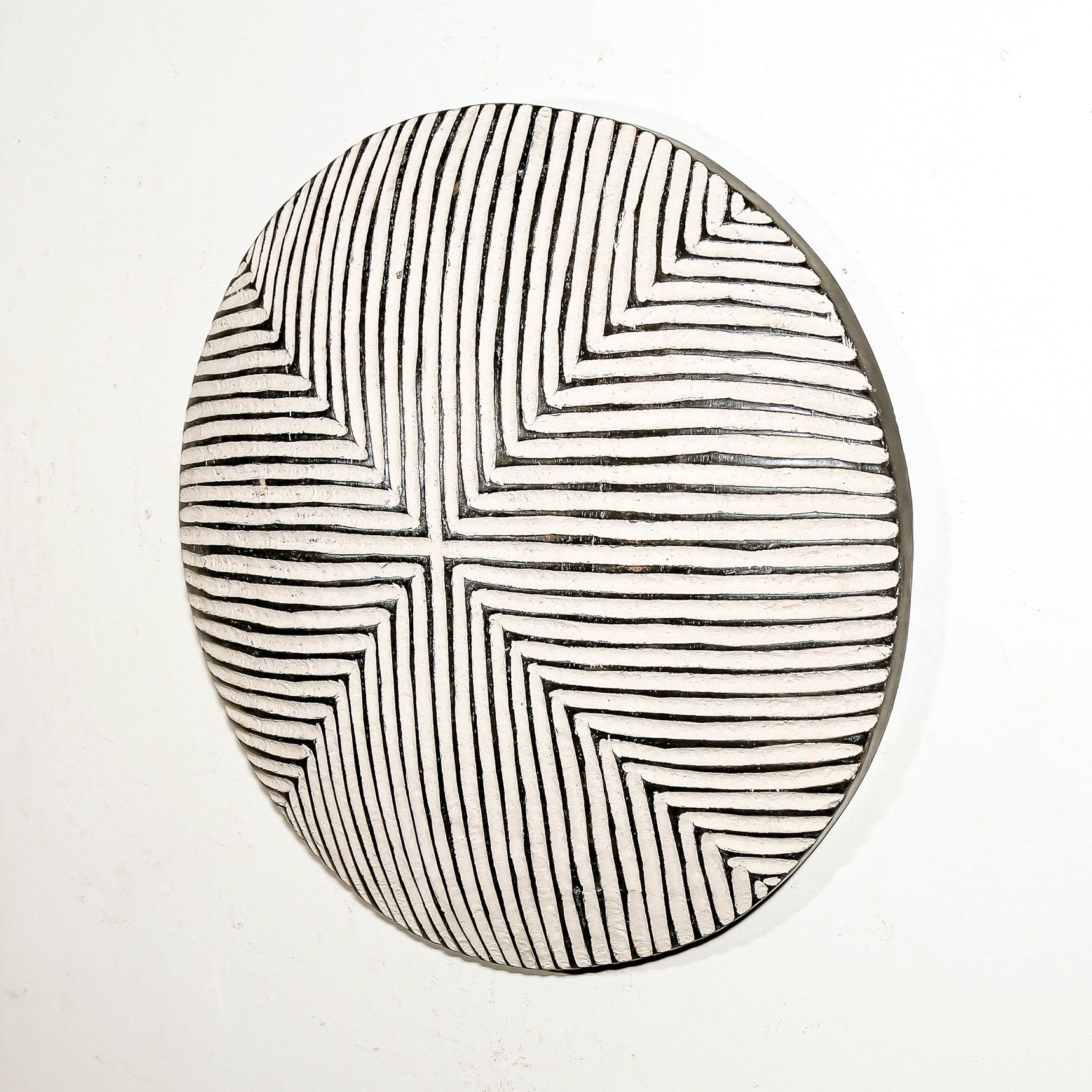 Round wood wall decor with rustic African traditional striped pattern on a white living room wall