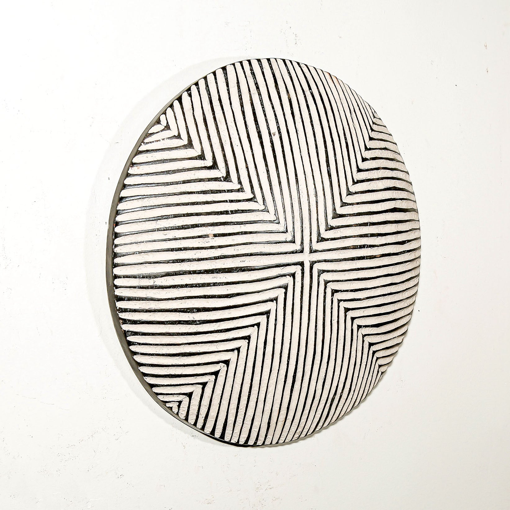 Round wood wall decor with rustic African traditional striped pattern on a white living room wall