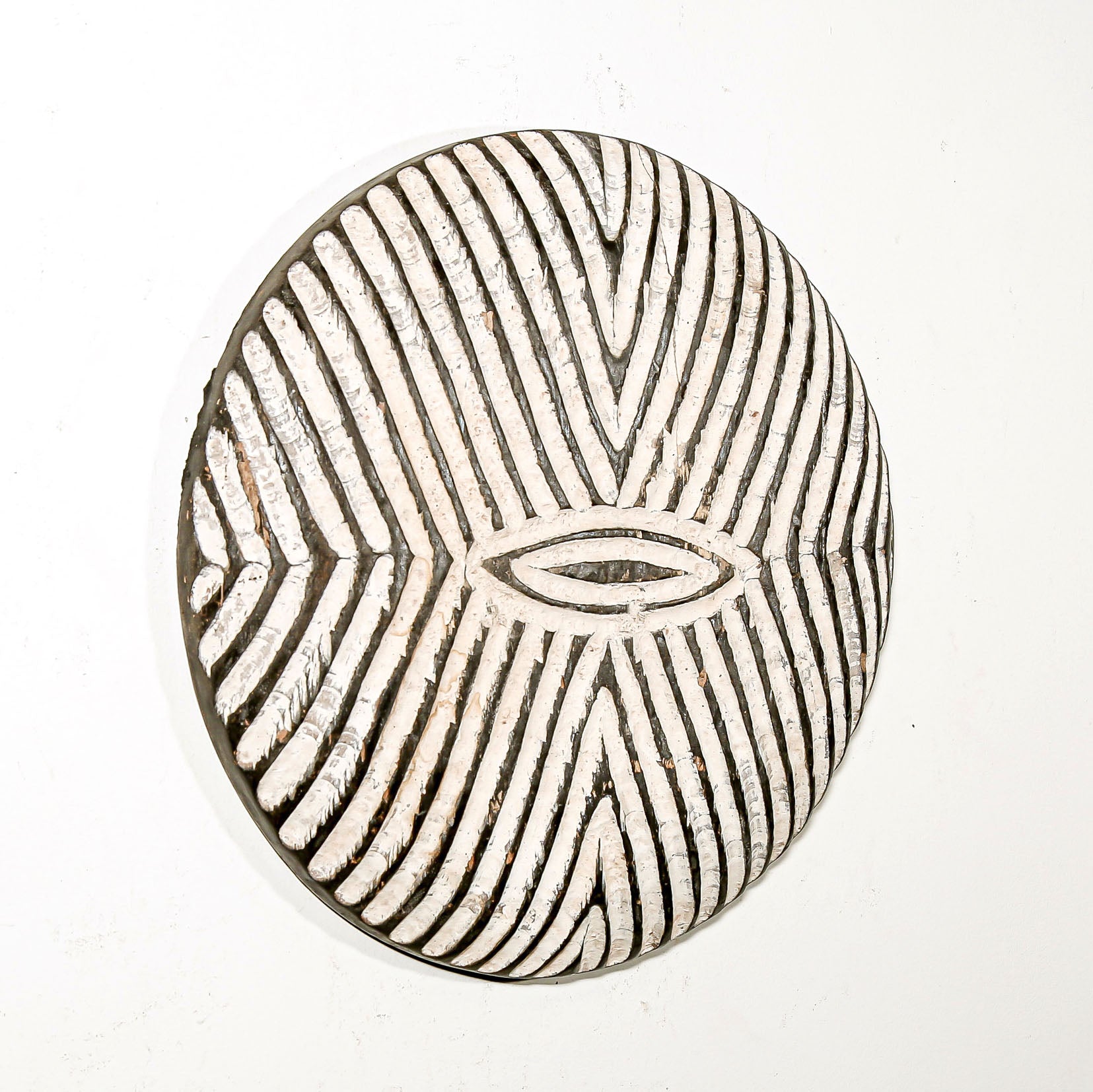Round wood wall decor with rustic African traditional striped pattern on a white living room wall