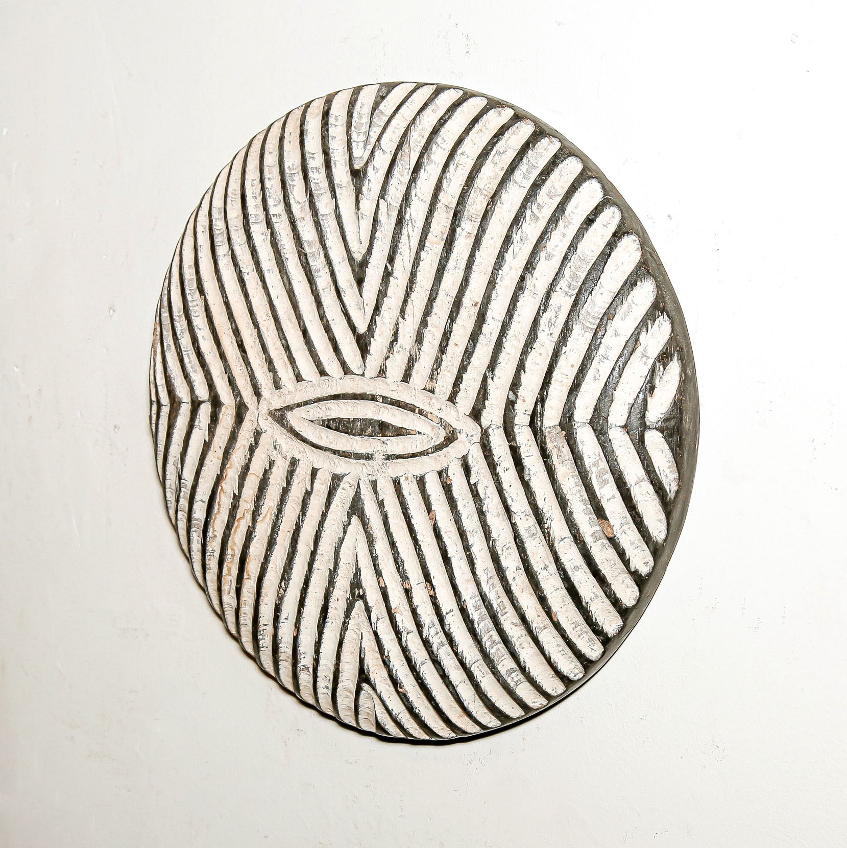 Round wood wall decor with rustic African traditional striped pattern on a white living room wall