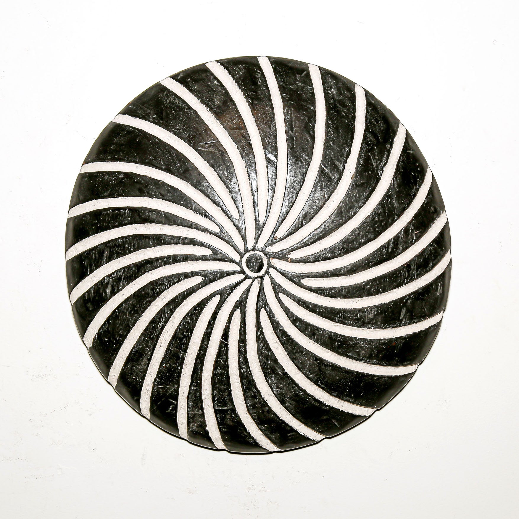 Round wood wall decor with rustic African traditional spiral pattern on a white living room wall