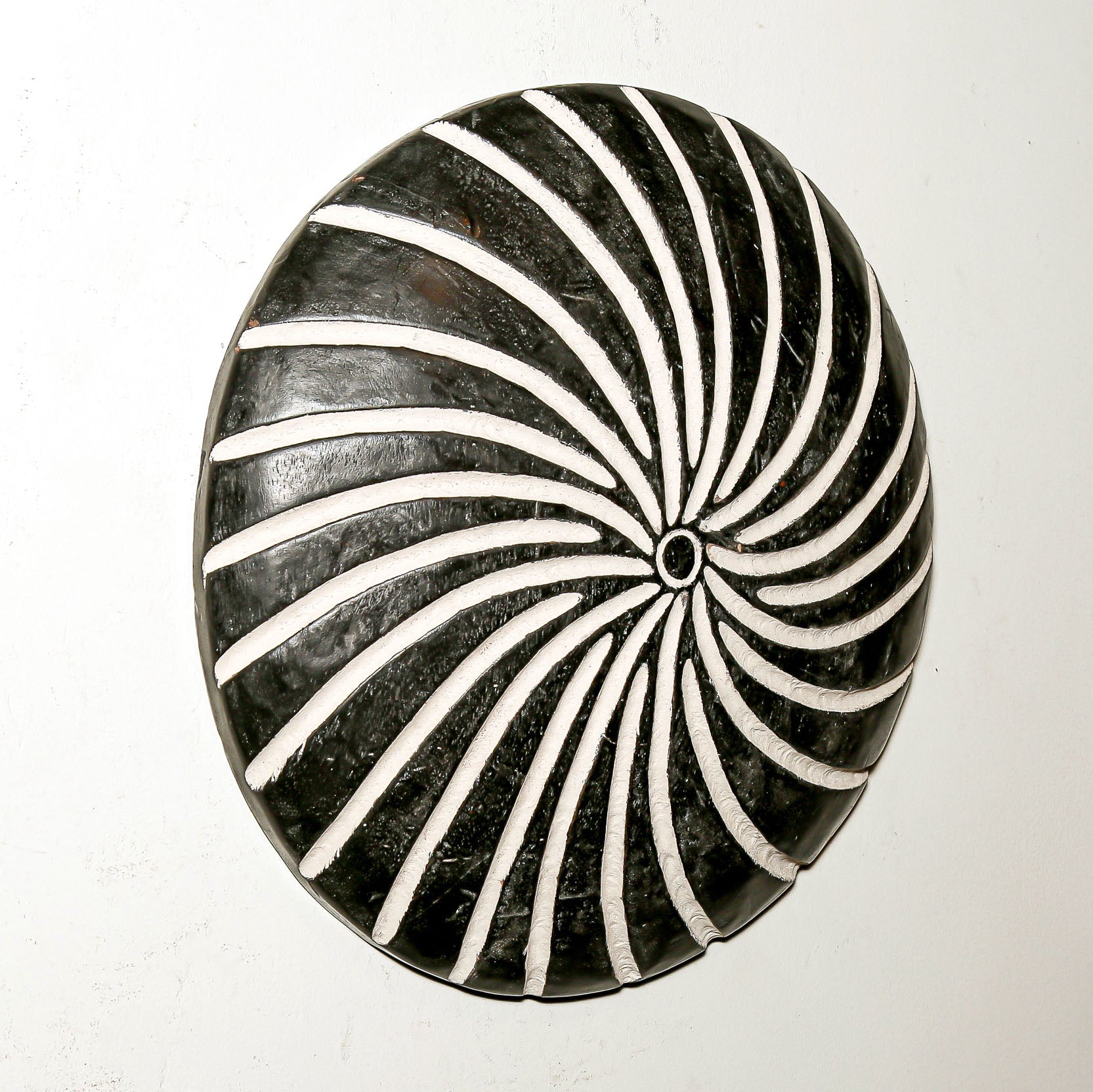 Round wood wall decor with rustic African traditional spiral pattern on a white living room wall