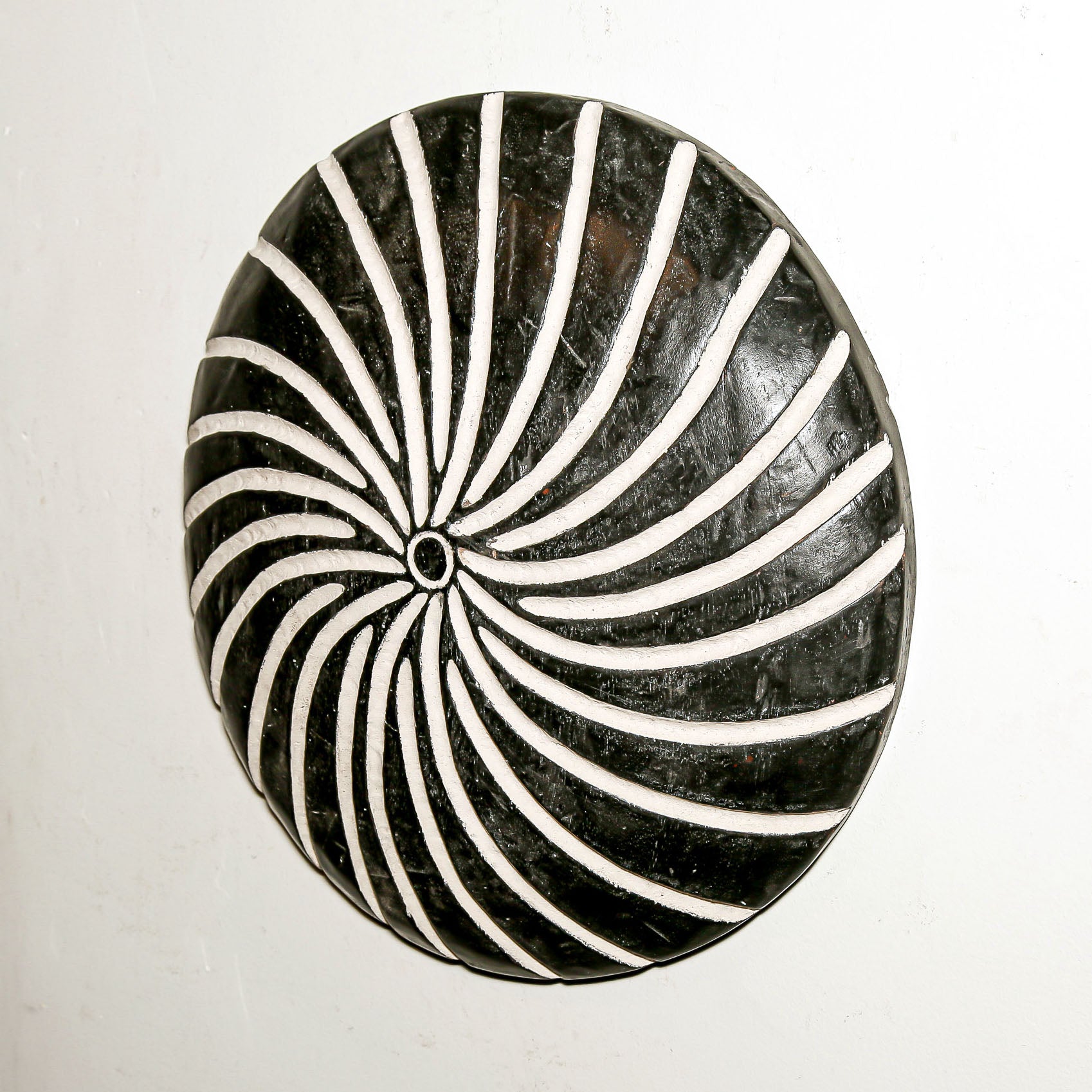 Round wood wall decor with rustic African traditional spiral pattern on a white living room wall