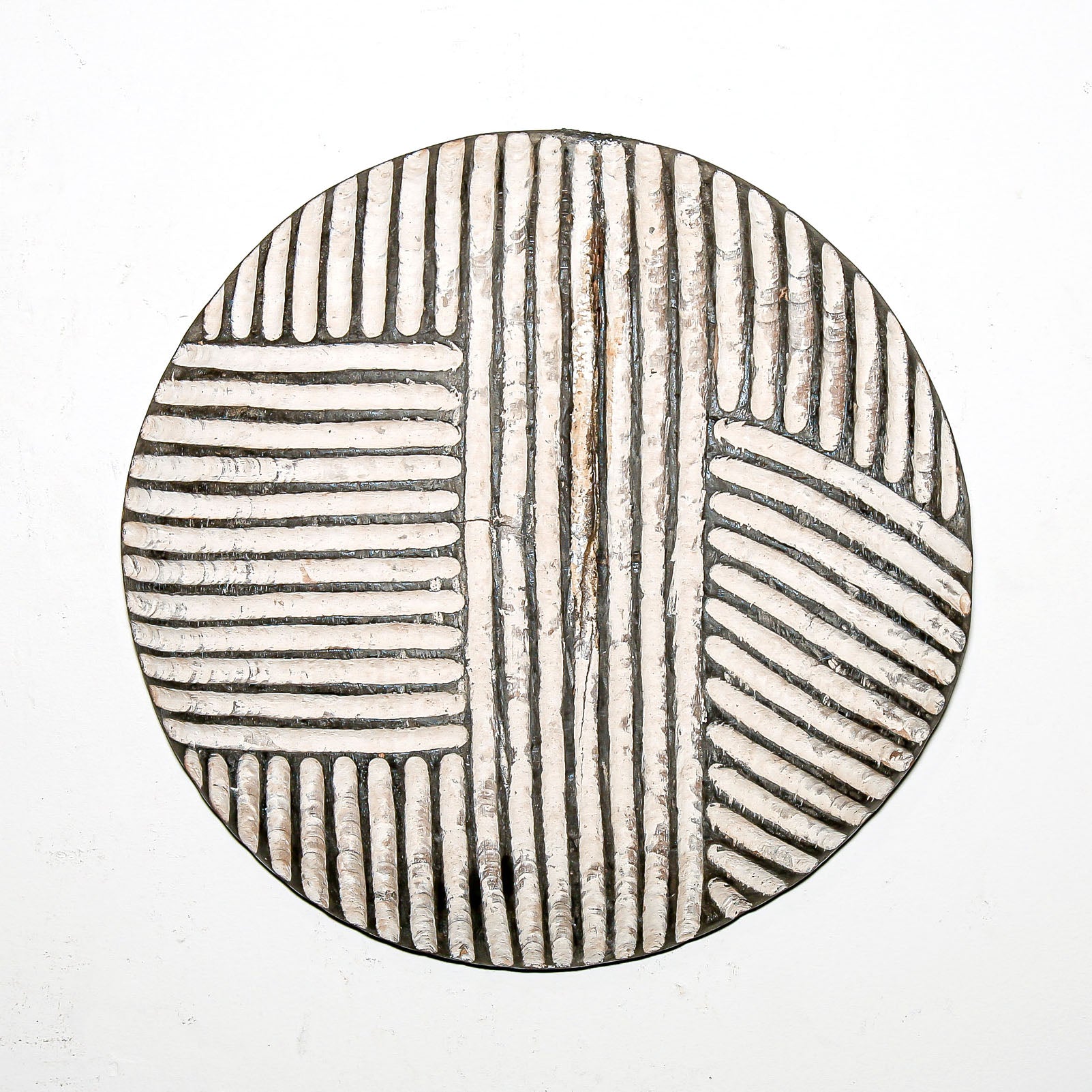 Round wood wall decor with rustic African traditional striped pattern on a white living room wall