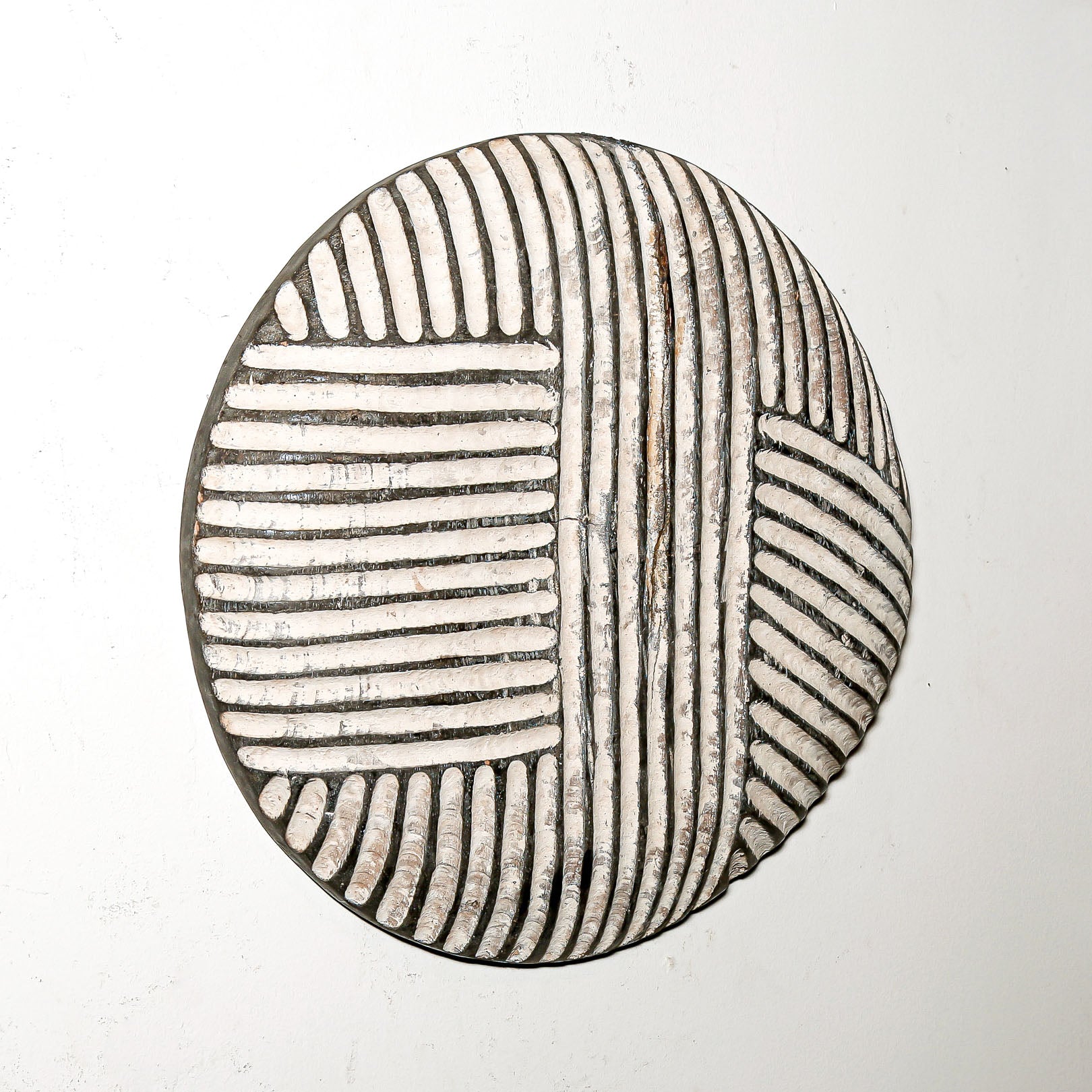 Round wood wall decor with rustic African traditional striped pattern on a white living room wall