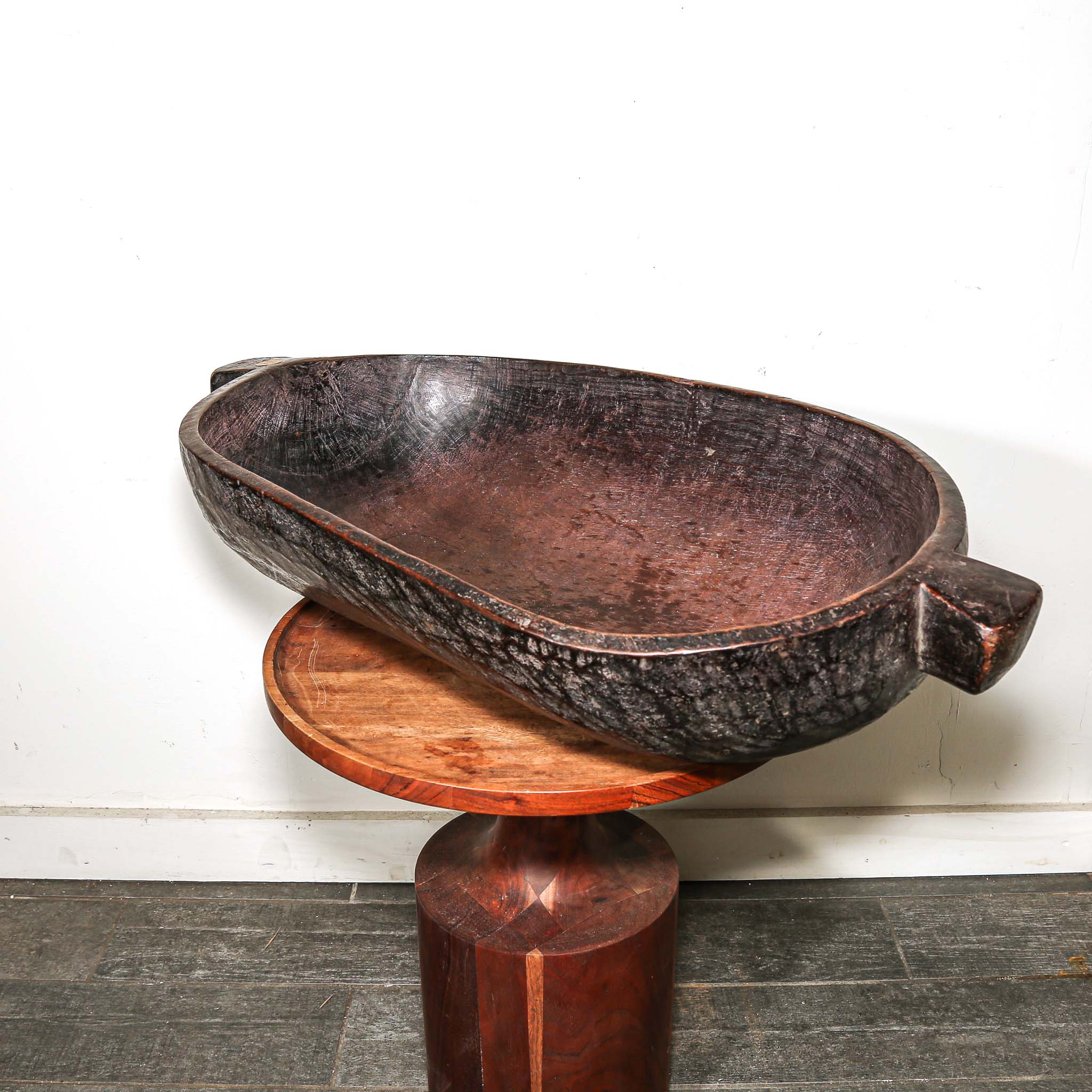 Decorative wooden vintage African oval bowl on a stand against a white wall