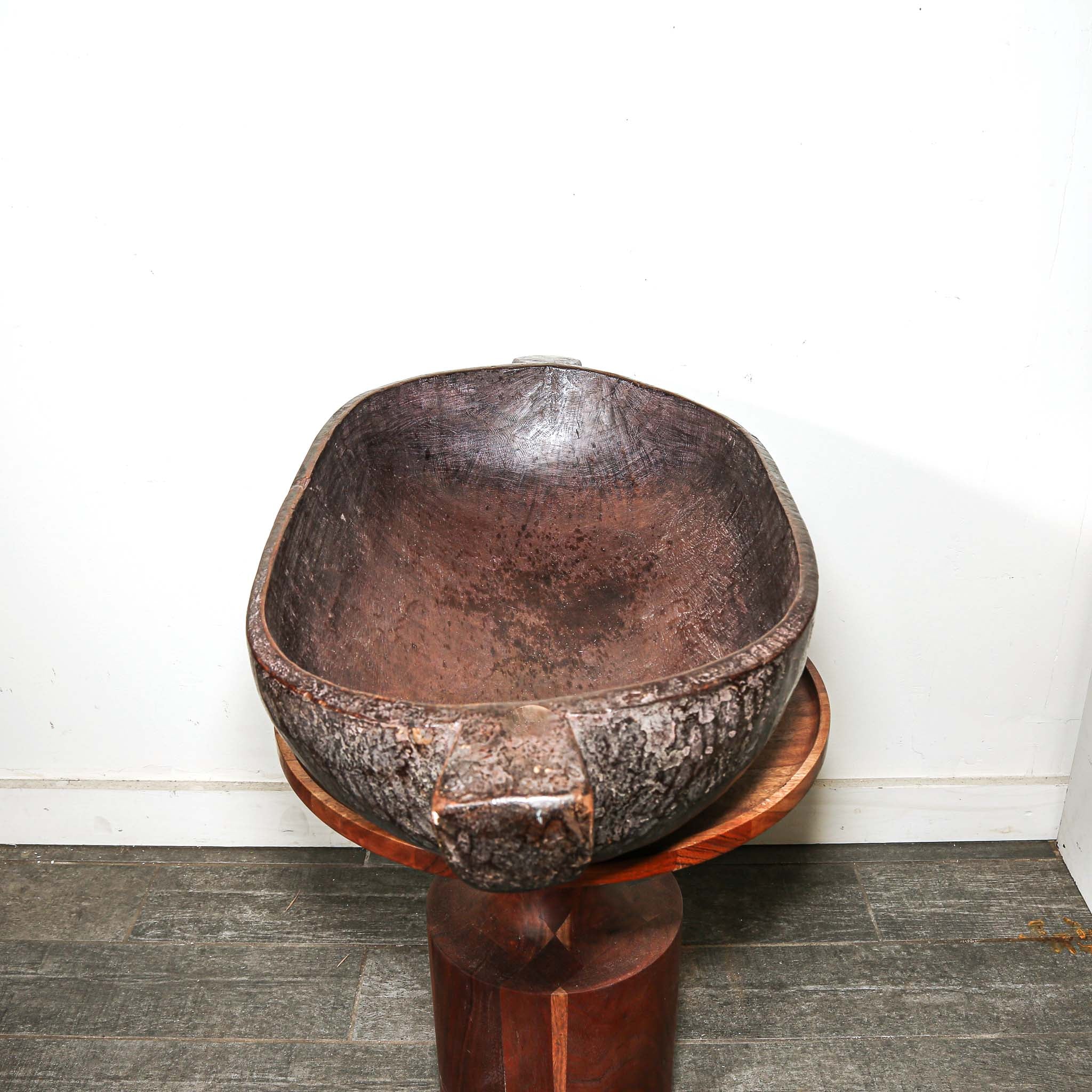 Decorative wooden vintage African oval bowl on a stand against a white wall