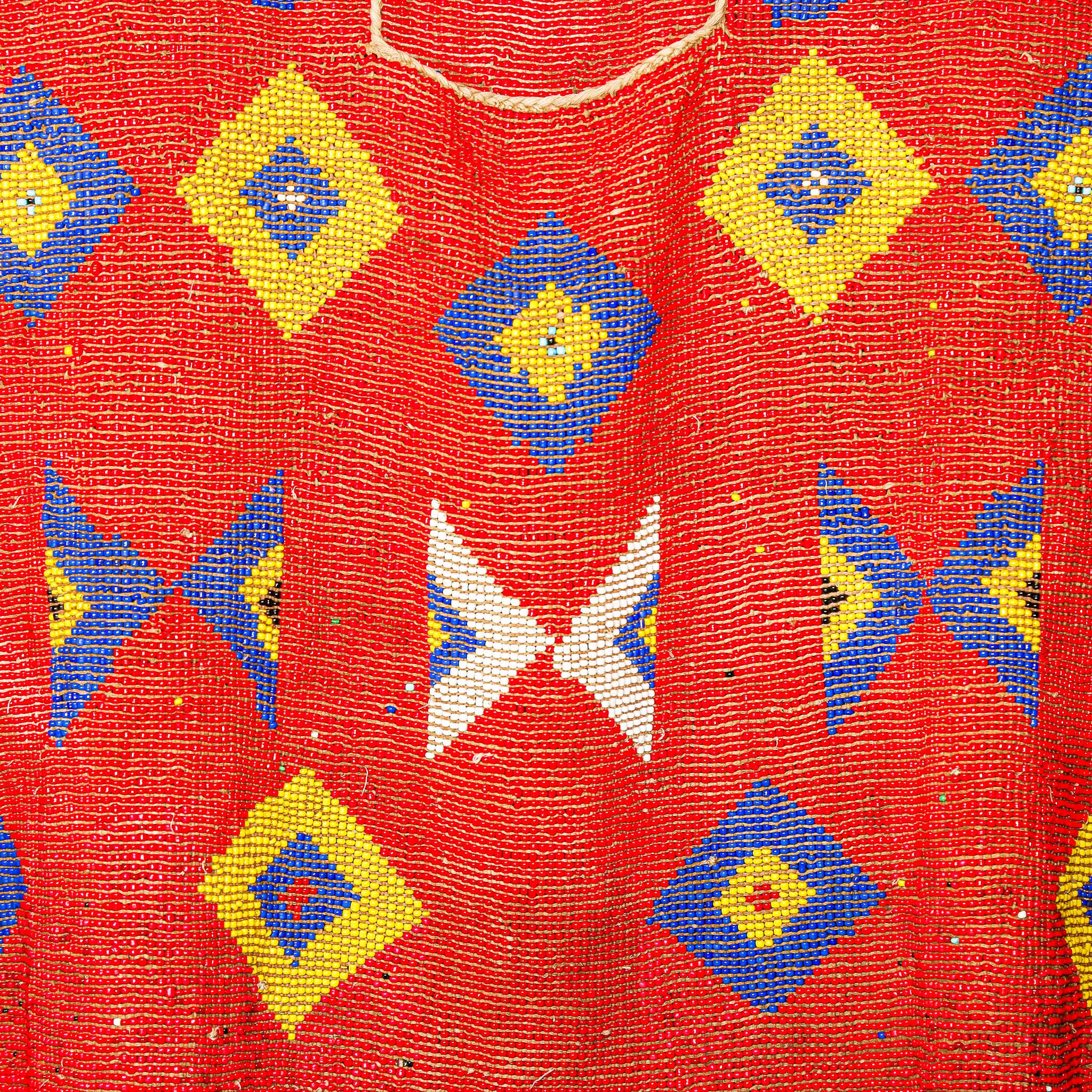 Red beaded garment for sculptural display with geometric patterns on a stand against a white background. high quality collectable African art