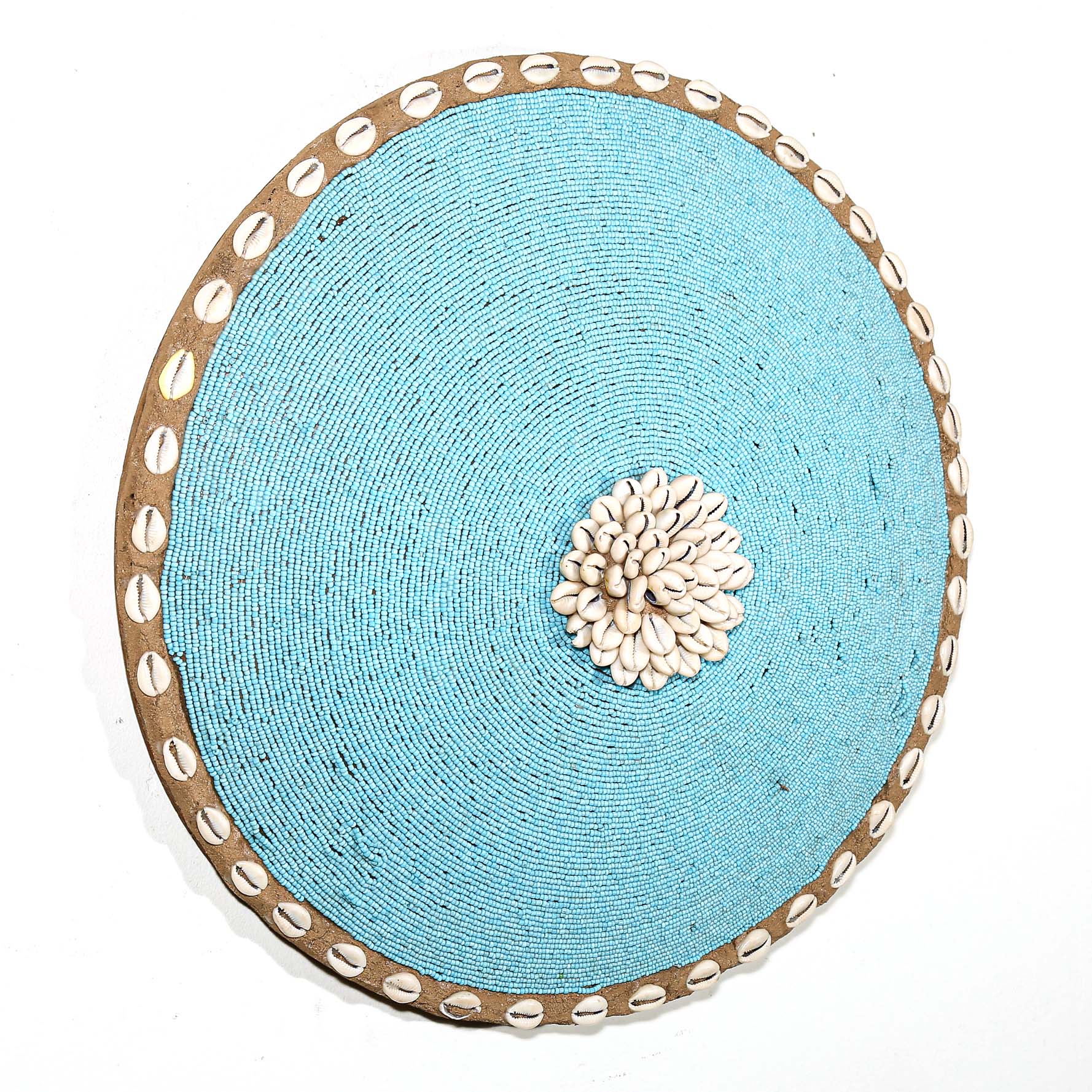 Round white beaded wall shield decor with a central white flower design made from cowrie shells hanging on a white wall.