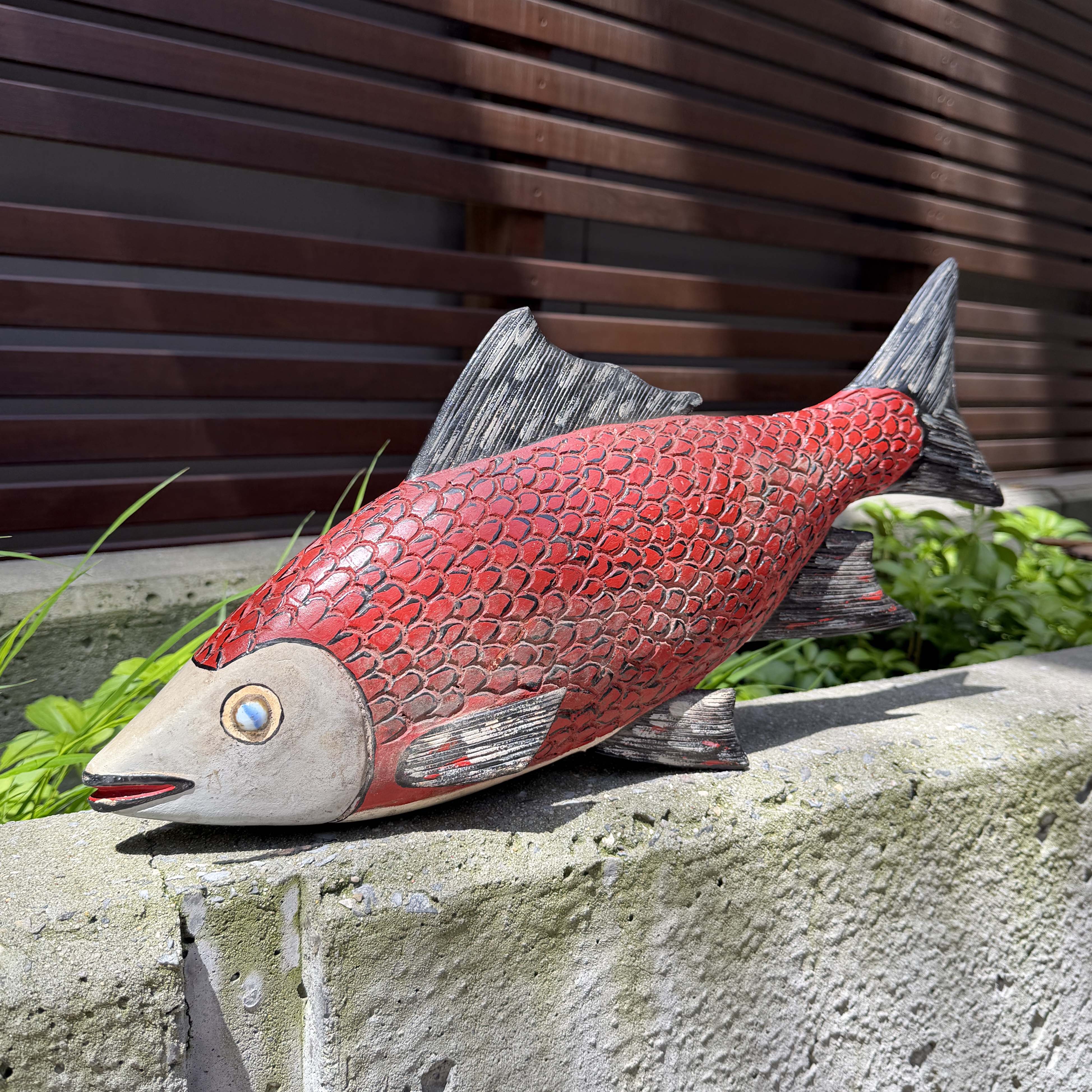 Red fish sculpture on a stone ledge with a wooden slat background