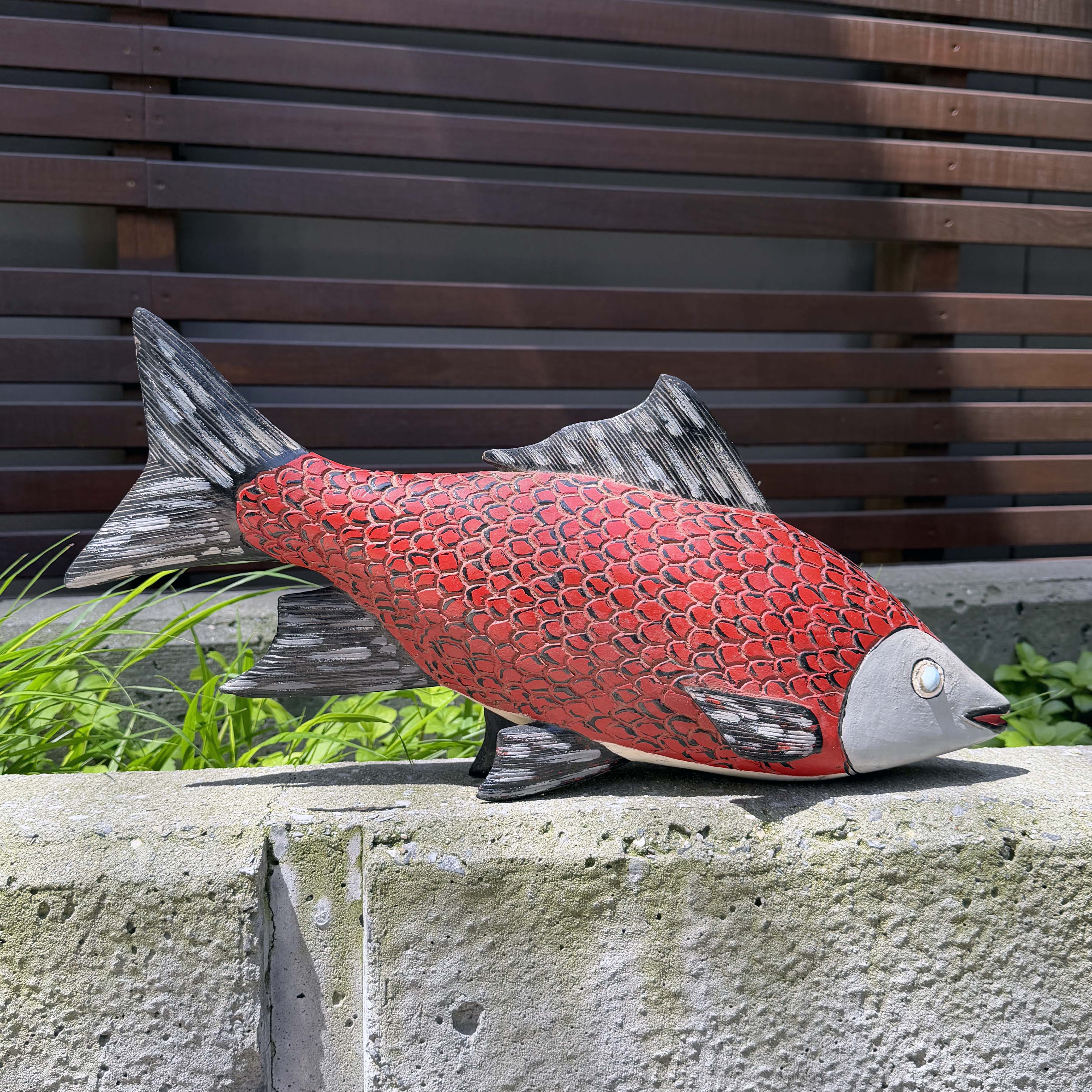 Red fish sculpture on a stone ledge with a wooden bench in the background