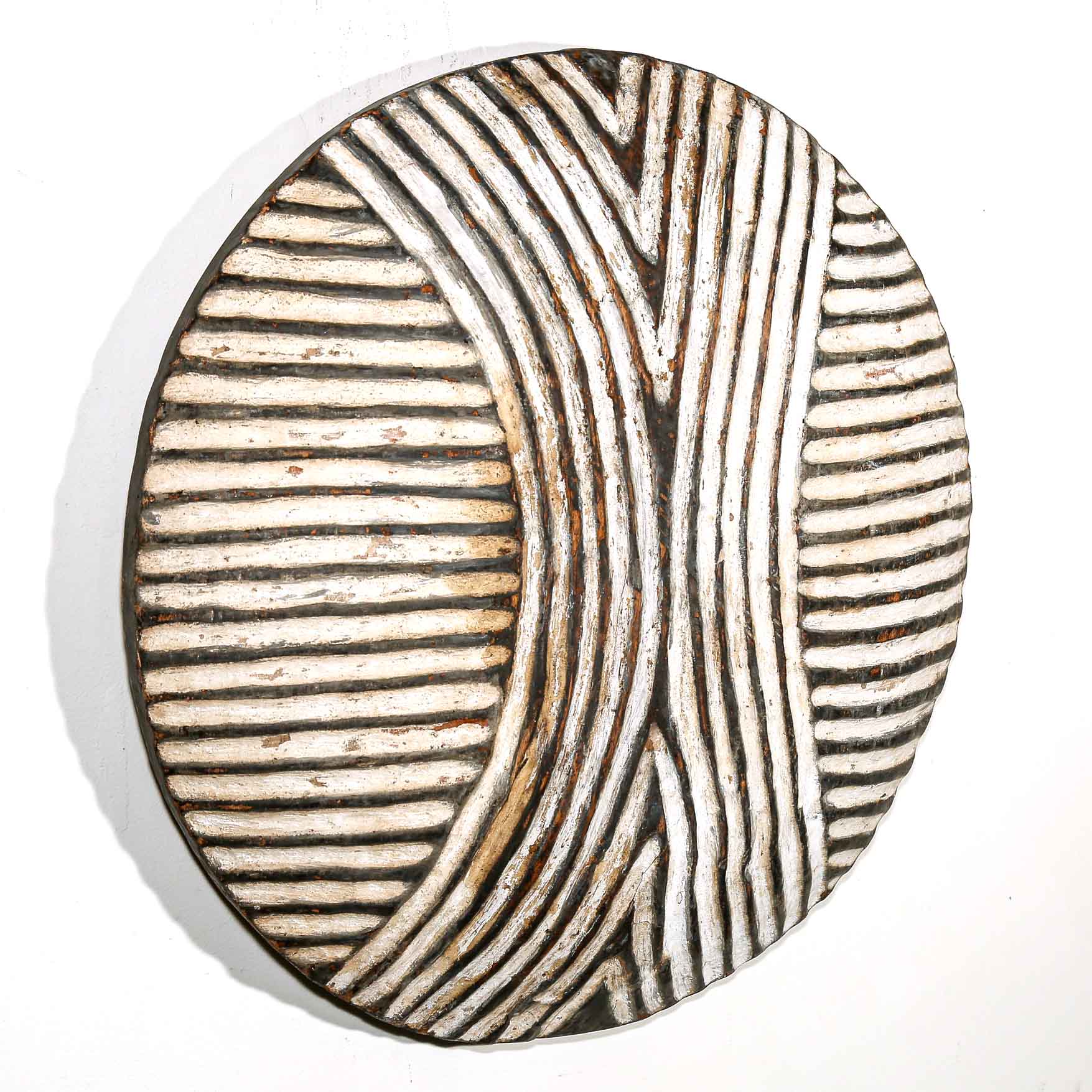 Round wooden wall hanging shield with black and white striped pattern on a white wall