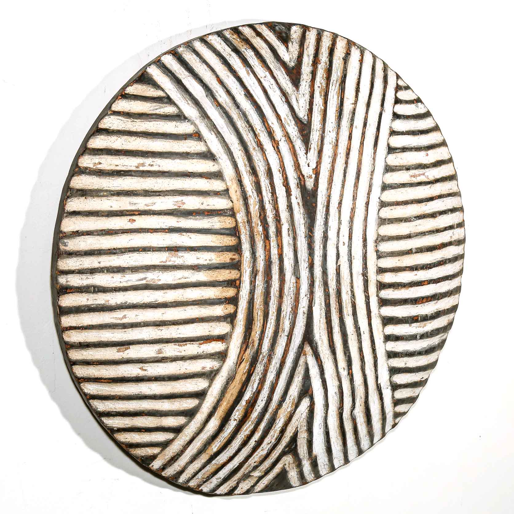 Round wooden wall hanging shield with black and white striped pattern on a white wall