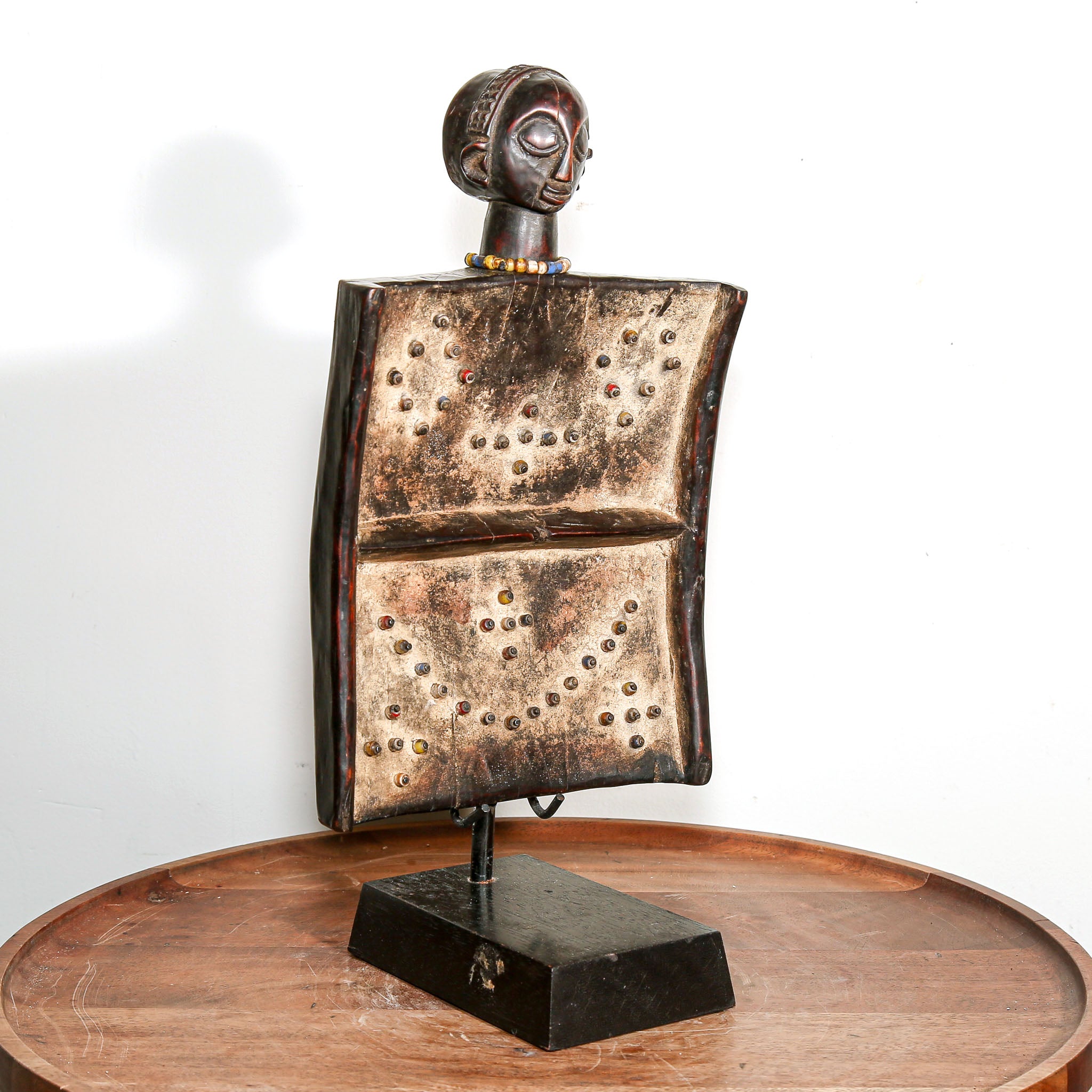 African wooden story telling art with metallic accents on a stand against a white background