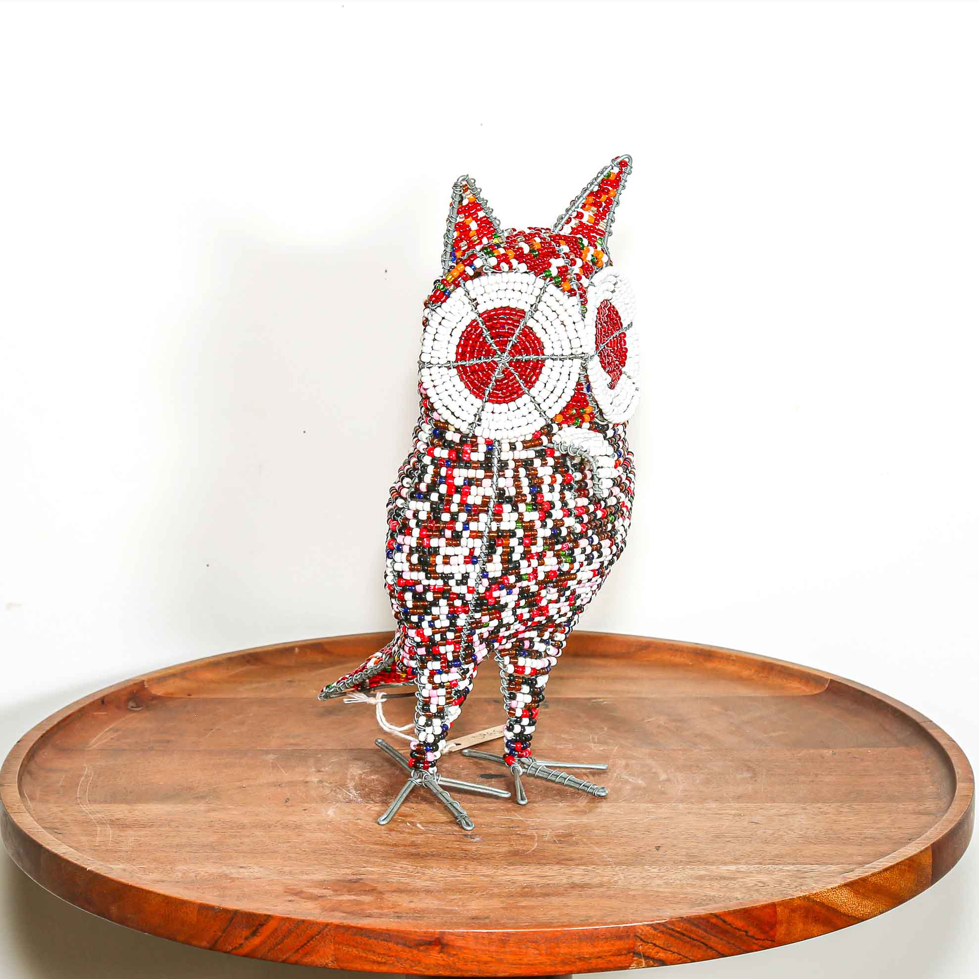 Decorative owl sculpture made out of colored beads from Africa on a wooden table with a white background.