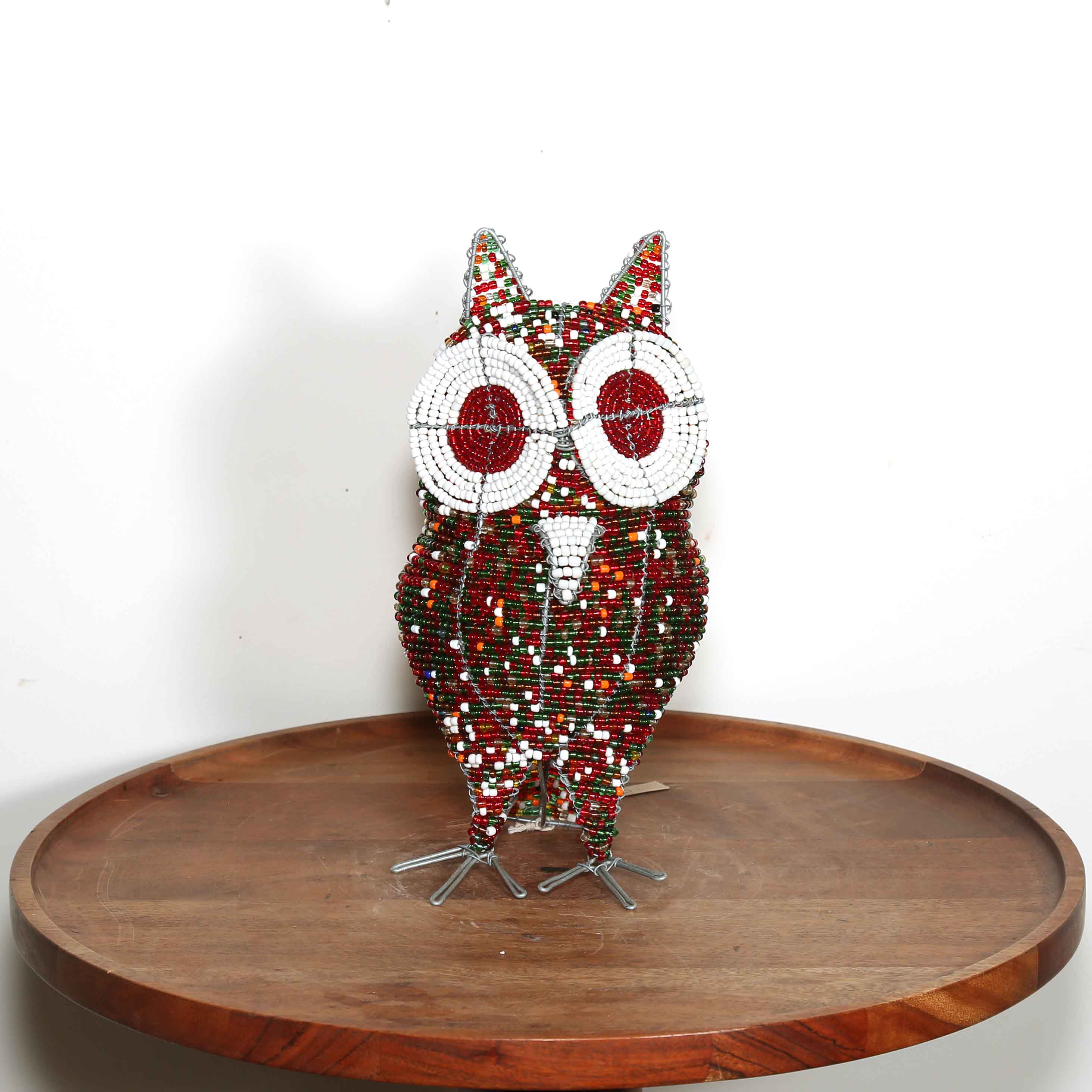 Decorative owl sculpture made out of colored beads from Africa on a wooden table with a white background.