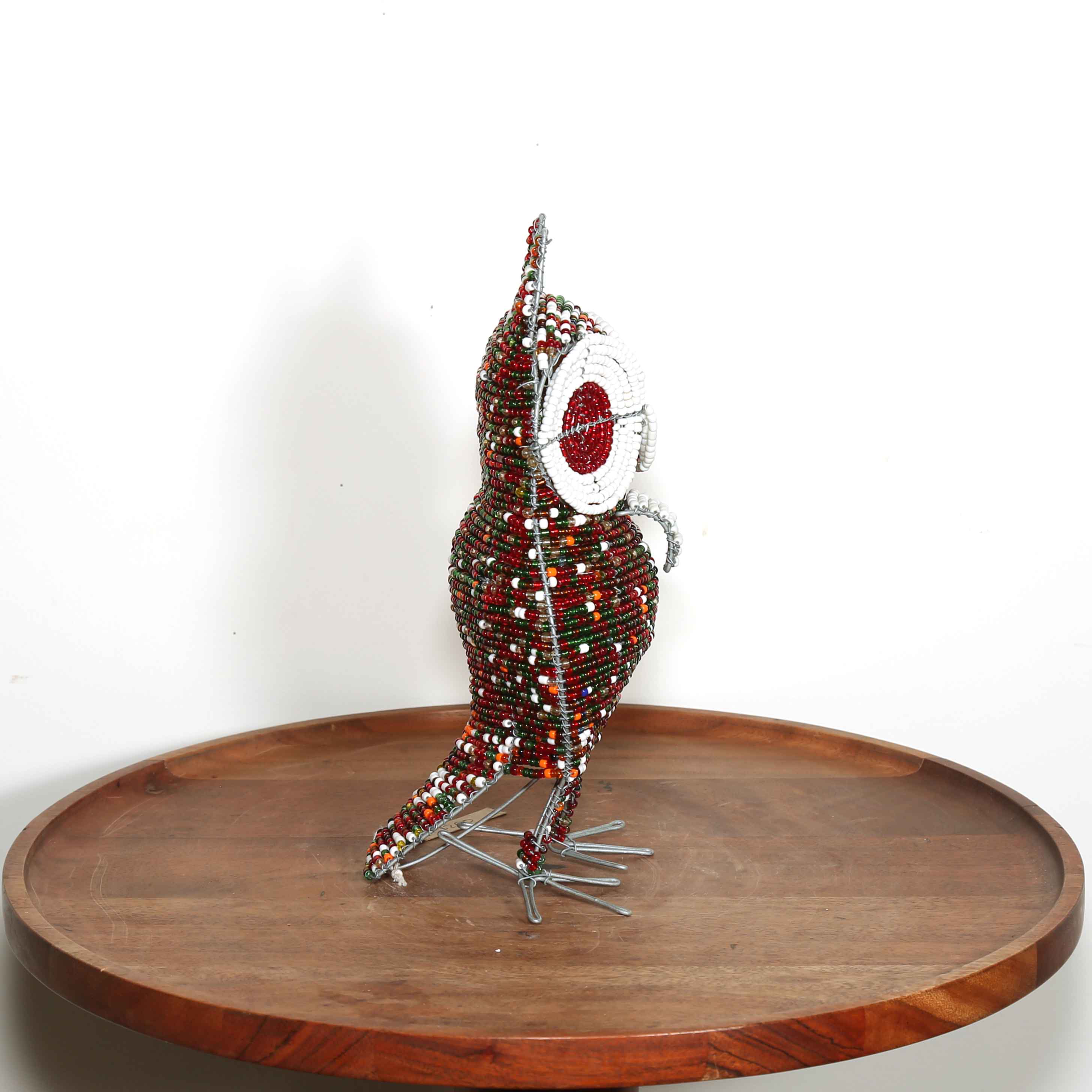 Decorative owl sculpture made out of colored beads from Africa on a wooden table with a white background.