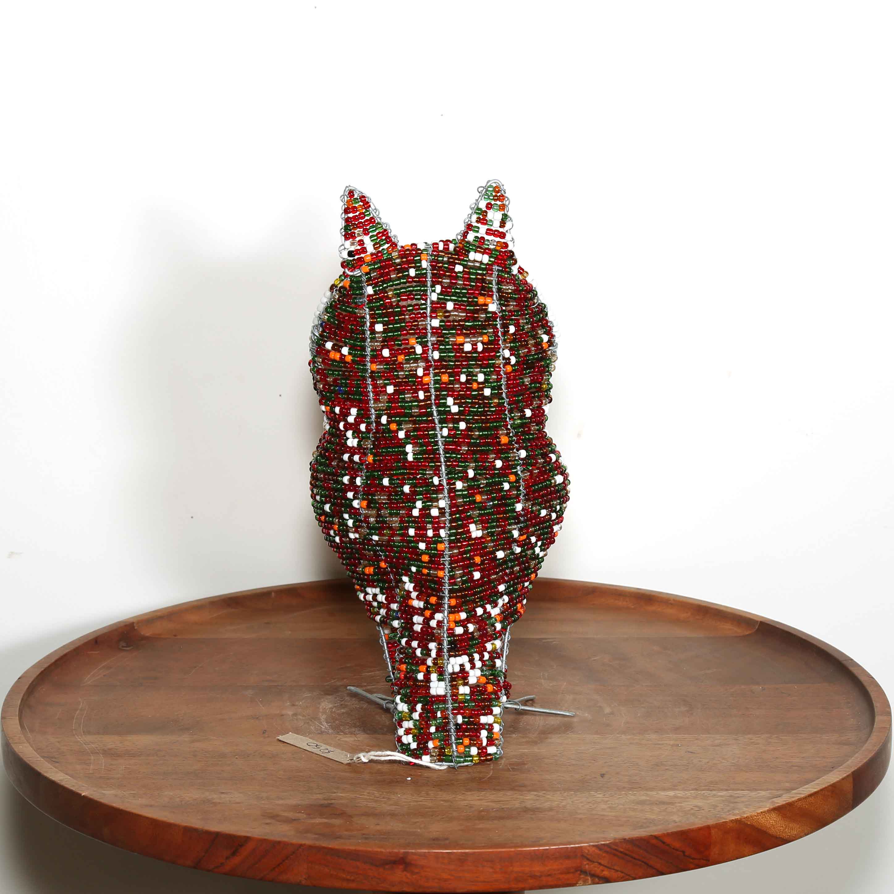 Decorative owl sculpture made out of colored beads from Africa on a wooden table with a white background.
