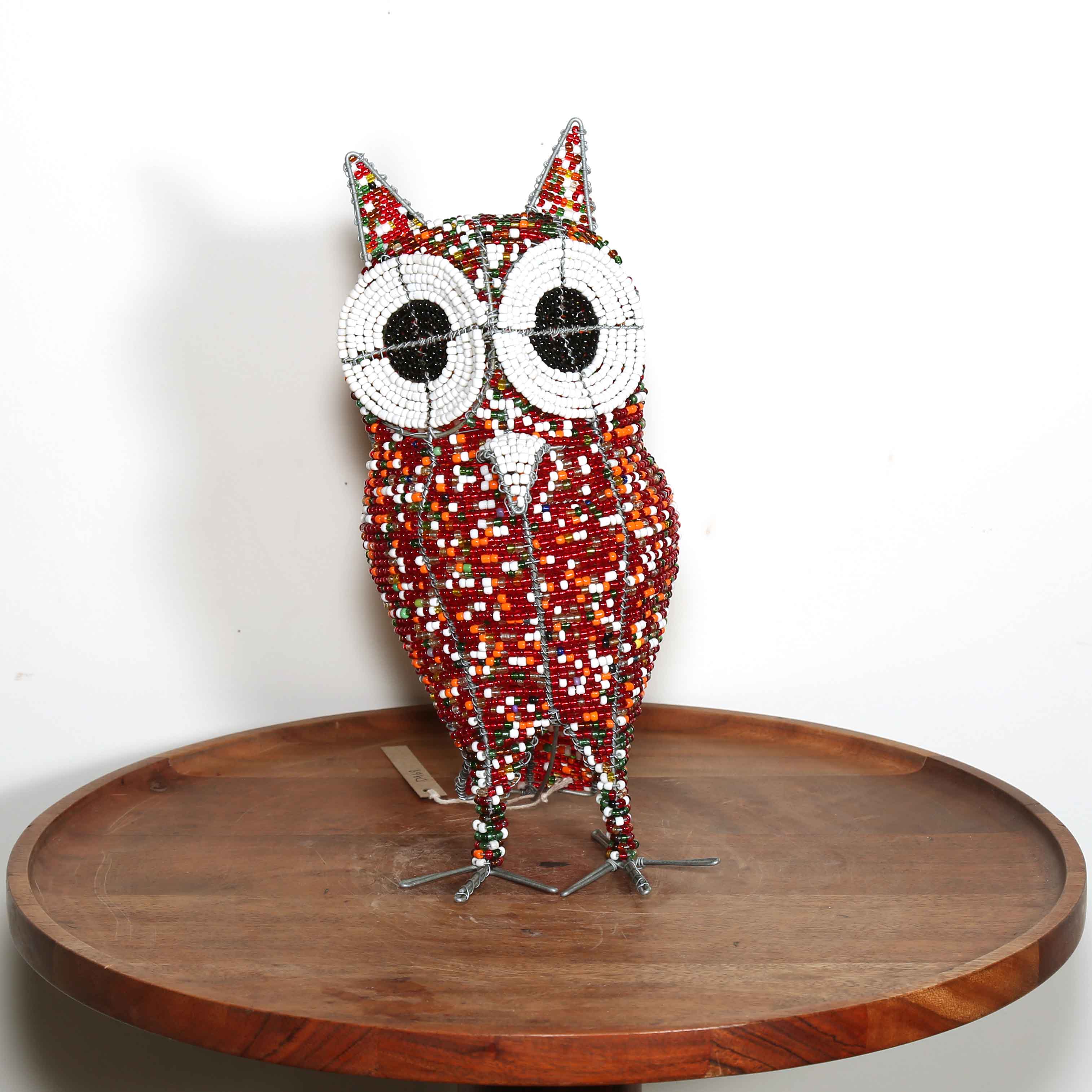 Decorative owl sculpture made out of colored beads from Africa on a wooden table with a white background.