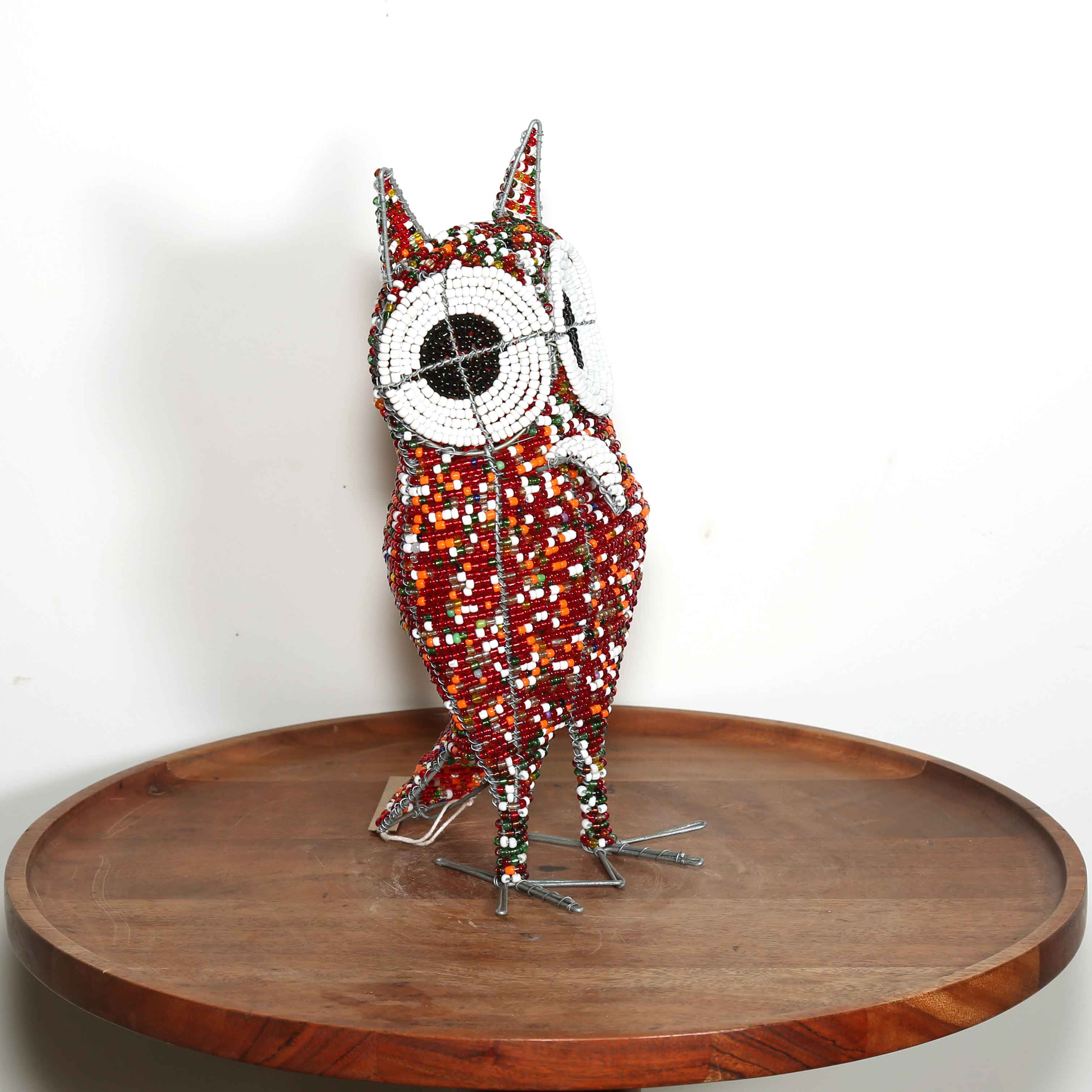 Decorative owl sculpture made out of colored beads from Africa on a wooden table with a white background.