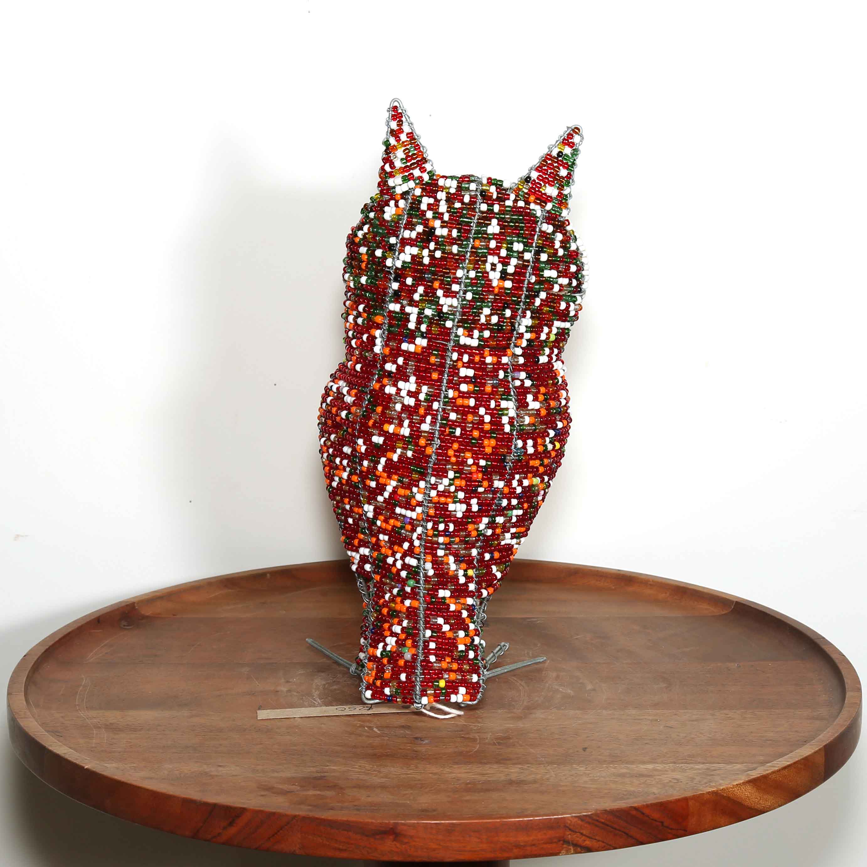 Decorative owl sculpture made out of colored beads from Africa on a wooden table with a white background.
