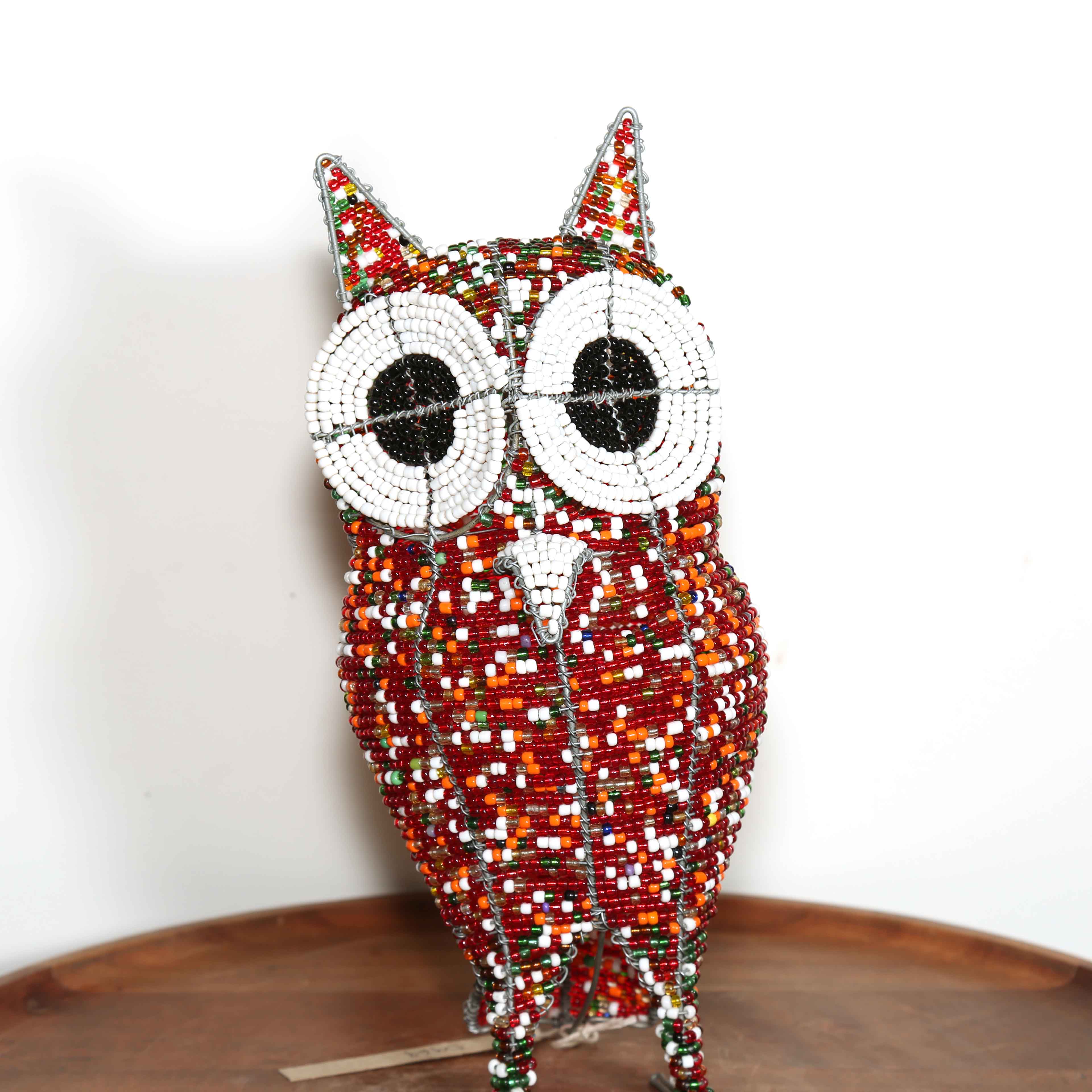 Decorative owl sculpture made out of colored beads from Africa on a wooden table with a white background.