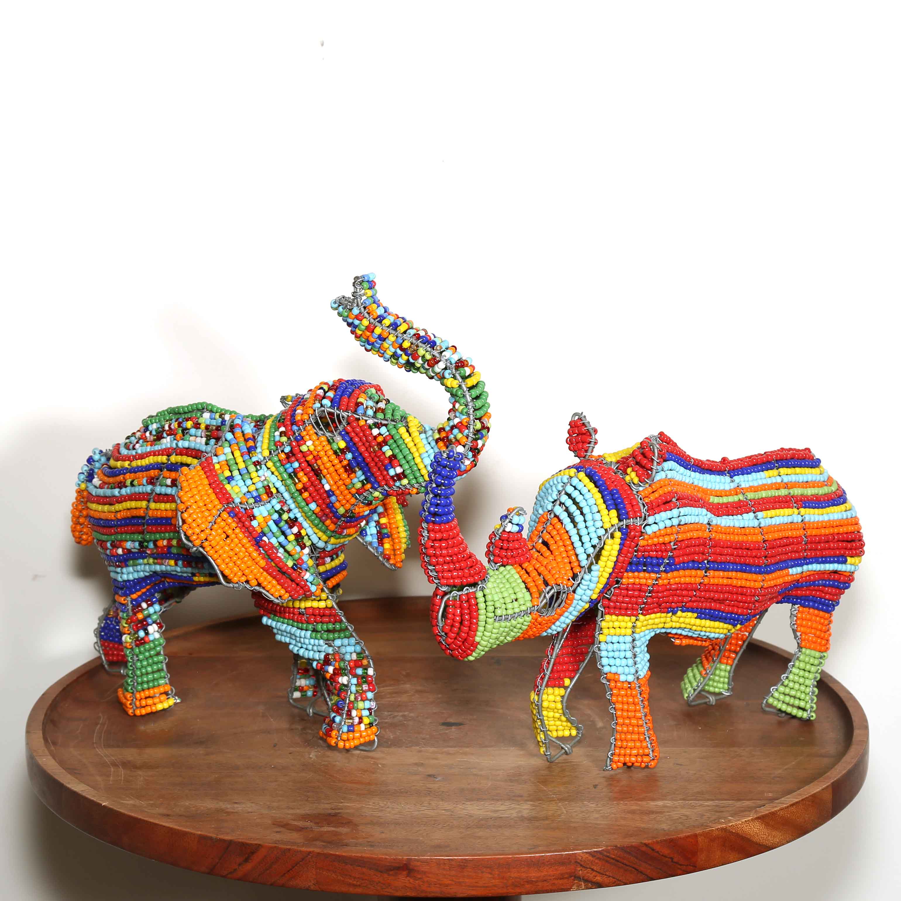 Colorful beaded elephant and rhino sculptures on a wooden platform with a white background
