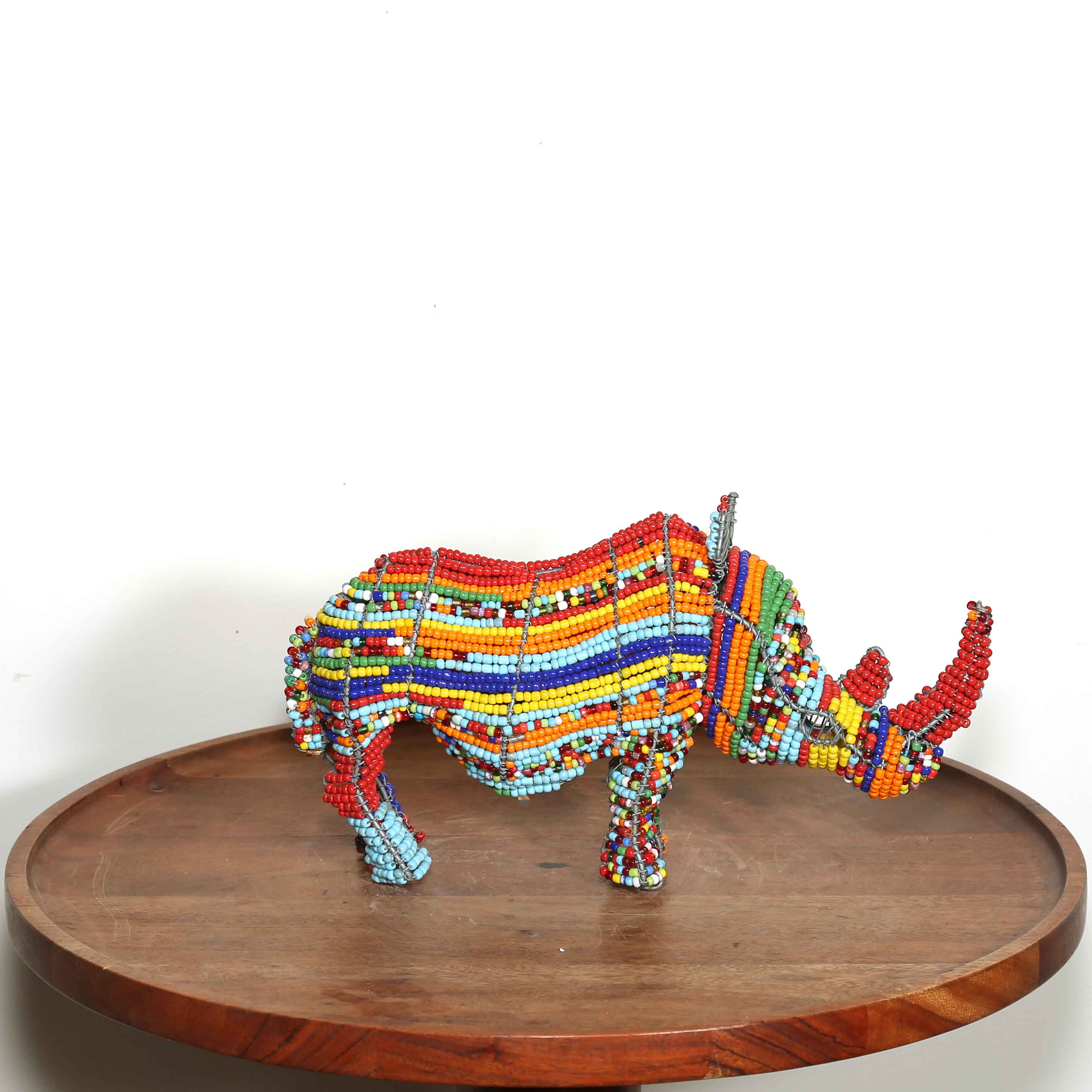 multicolored beaded rhino sculpture on a wooden platform with a white background