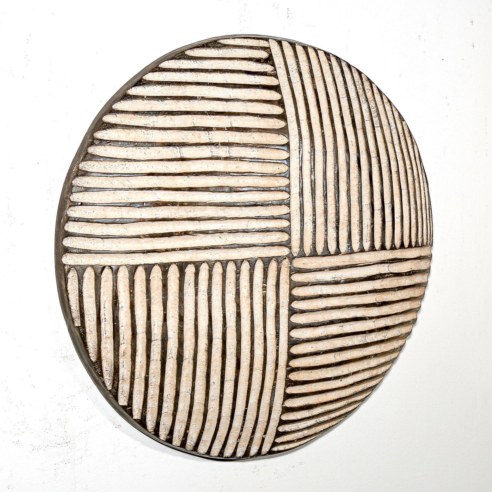 Round wood wall decor with rustic African traditional striped pattern on a white living room wall