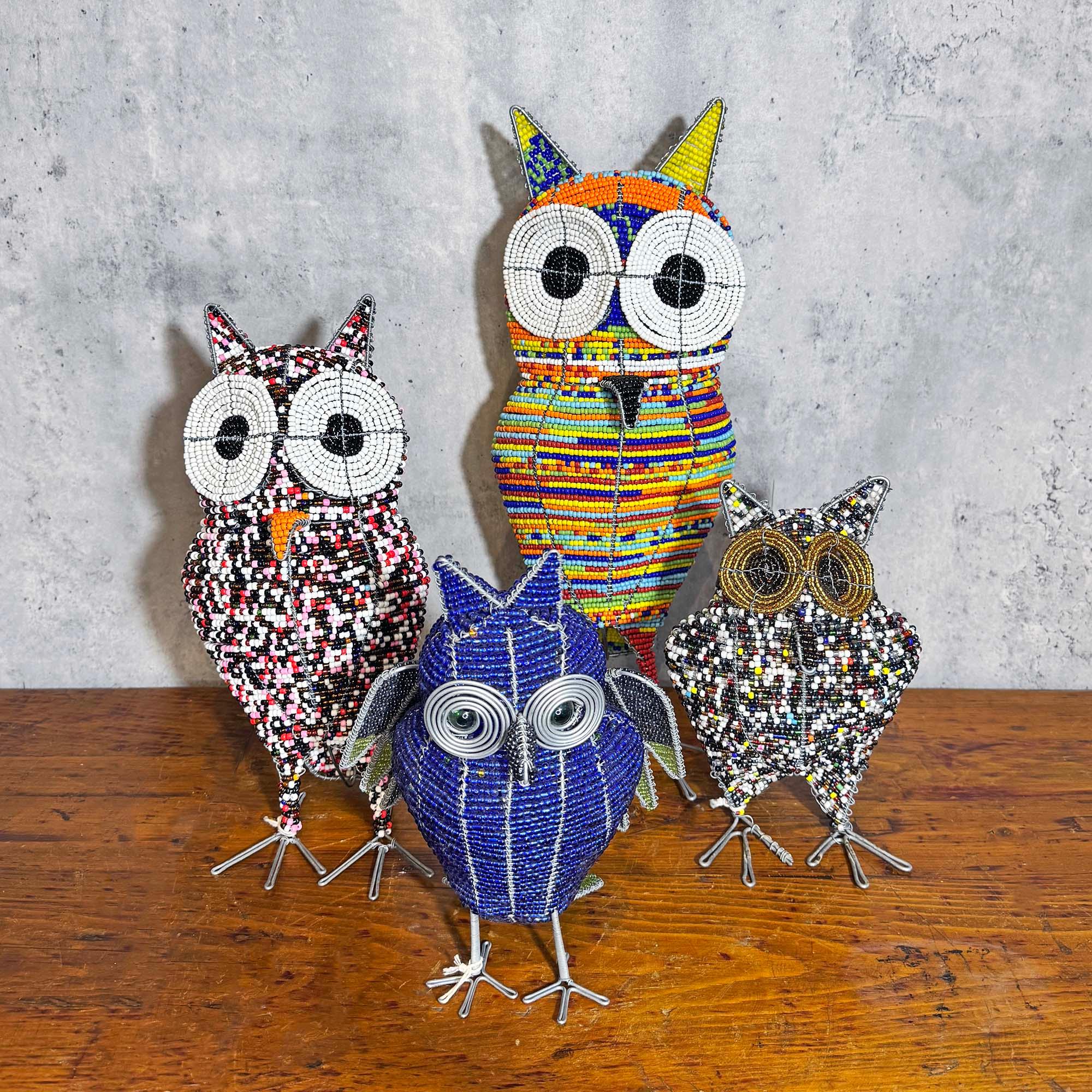Four colorful owl sculptures on a wooden surface with a concrete wall background